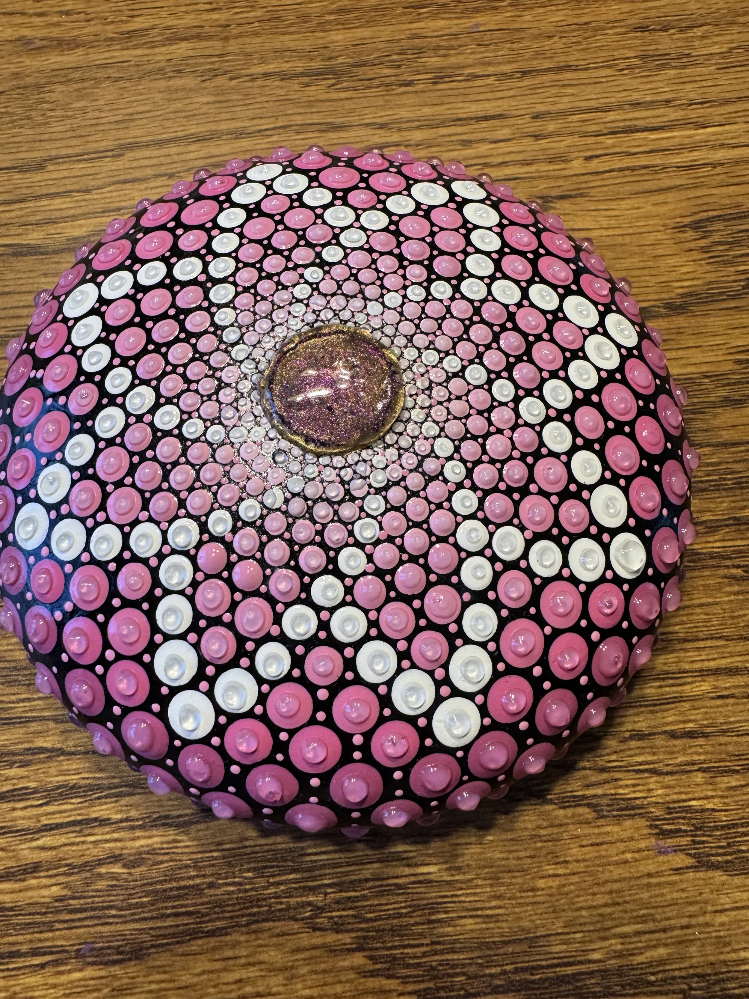 Decorative glass paperweight with a pink, white, and black dot pattern, on a wooden surface.