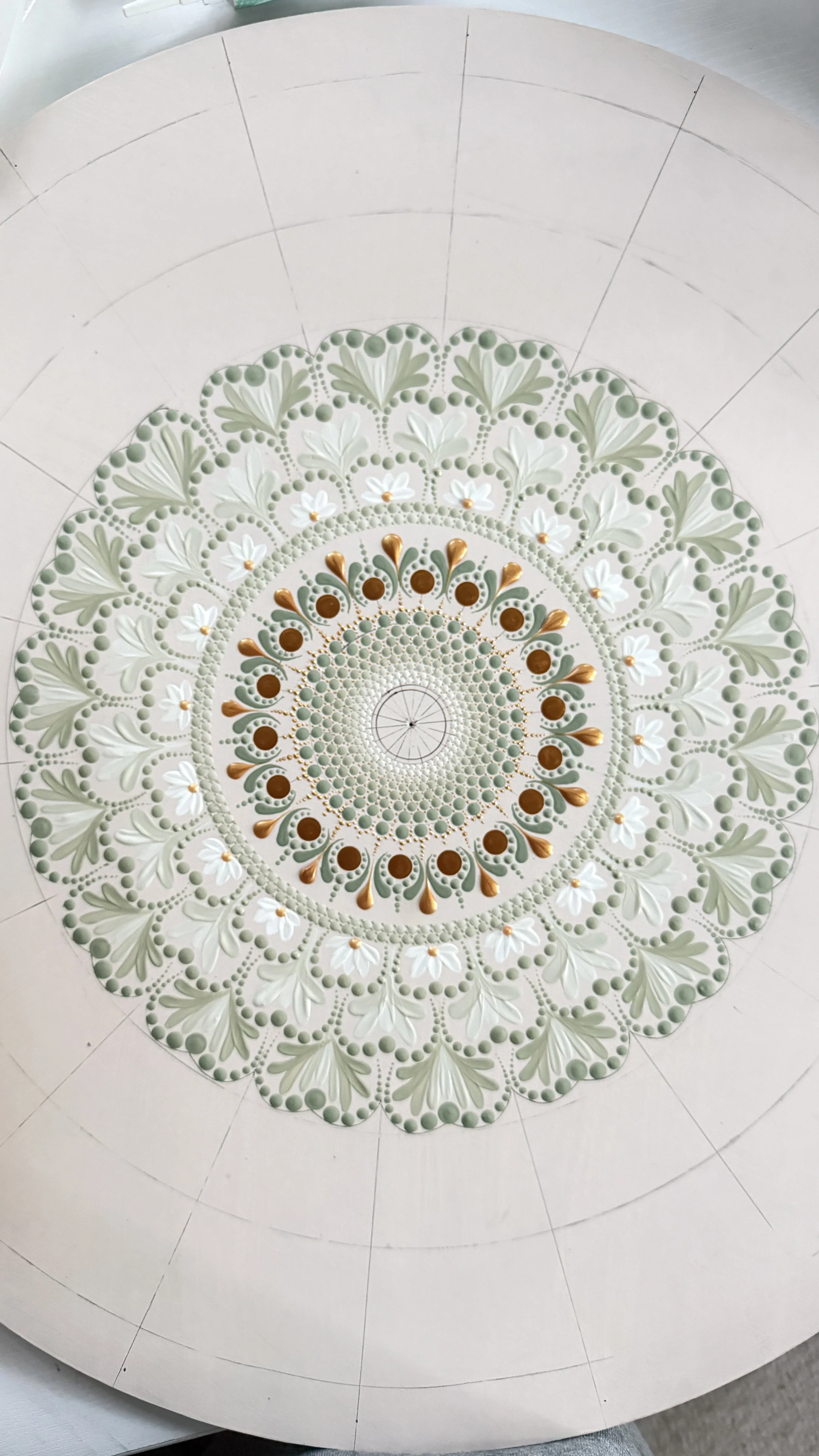 Circular decorative design with layered floral and leaf patterns in shades of cream, green, and gold.