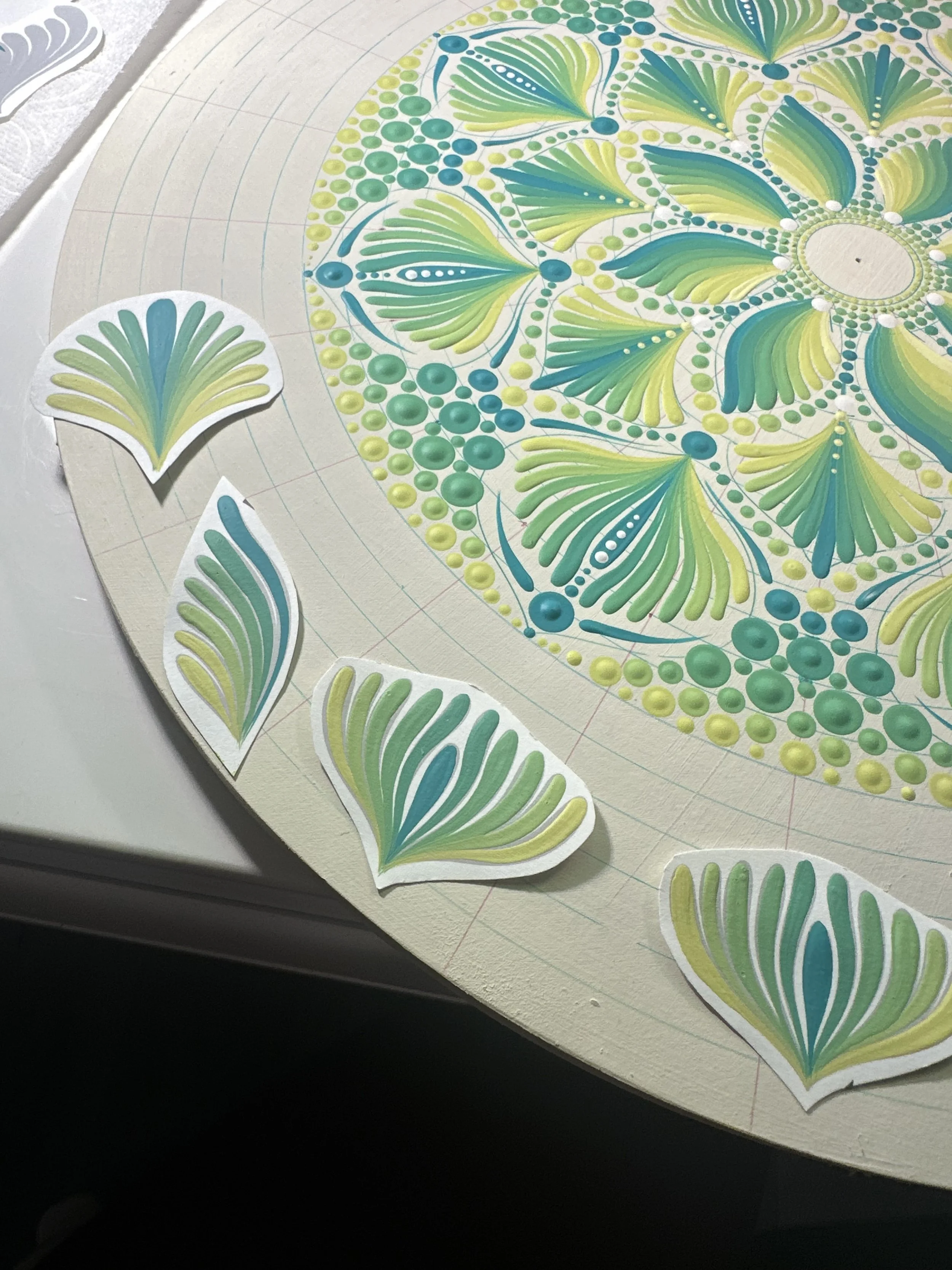 Colorful mandala design with leaf and dot patterns on a round surface, with several paper cutouts of the same design around it.
