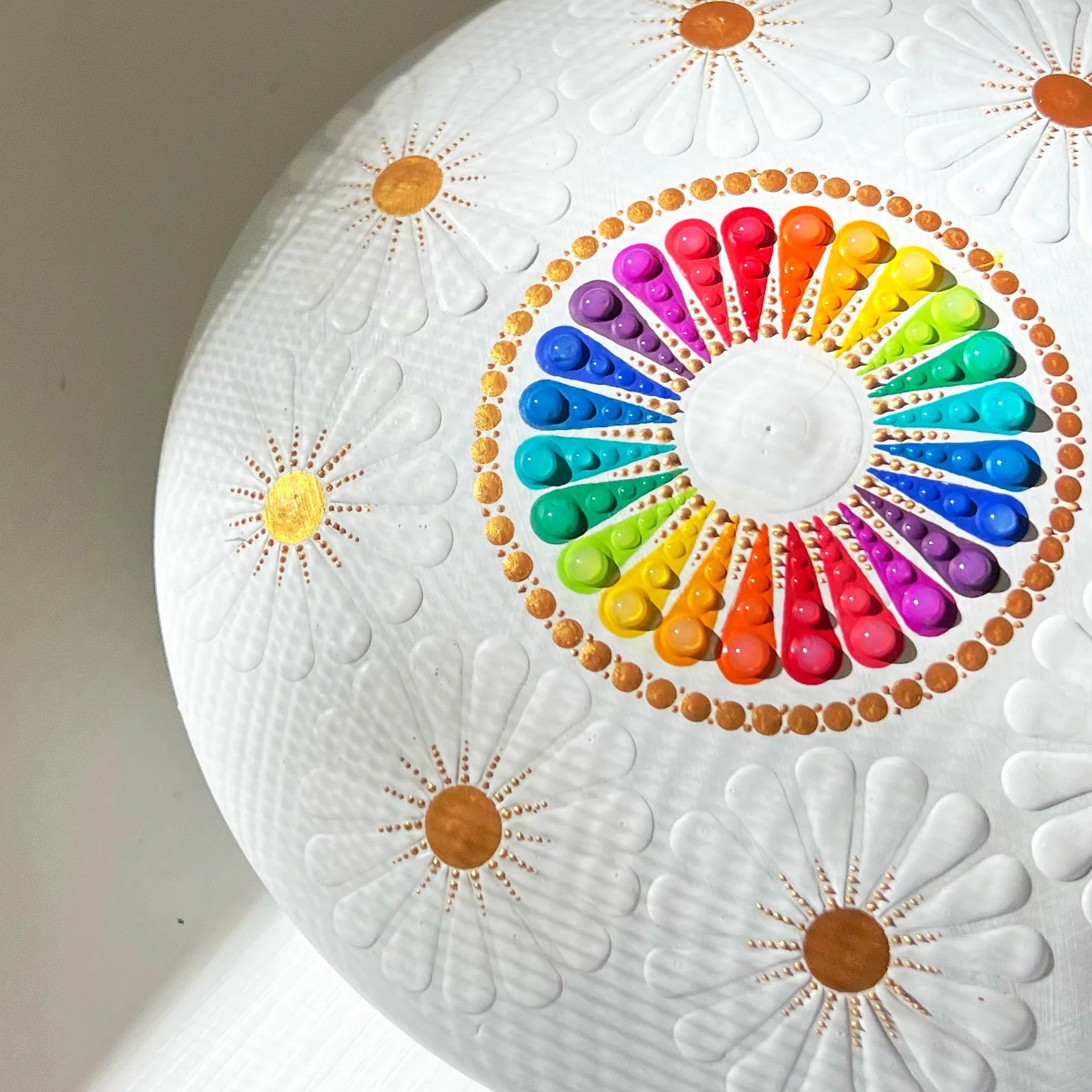 A white decorative paper parasol with orange daisy flower designs and a rainbow-colored pattern of thumbtacks arranged in a circle.
