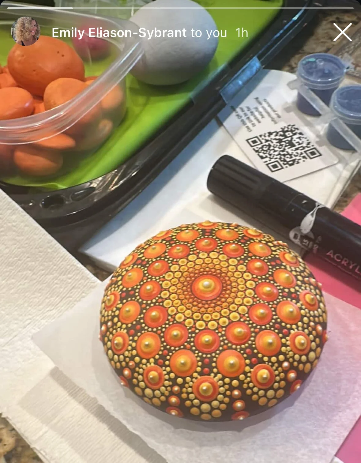 Colorful painted rock with concentric patterns of orange, yellow, and black, placed on a white paper napkin.