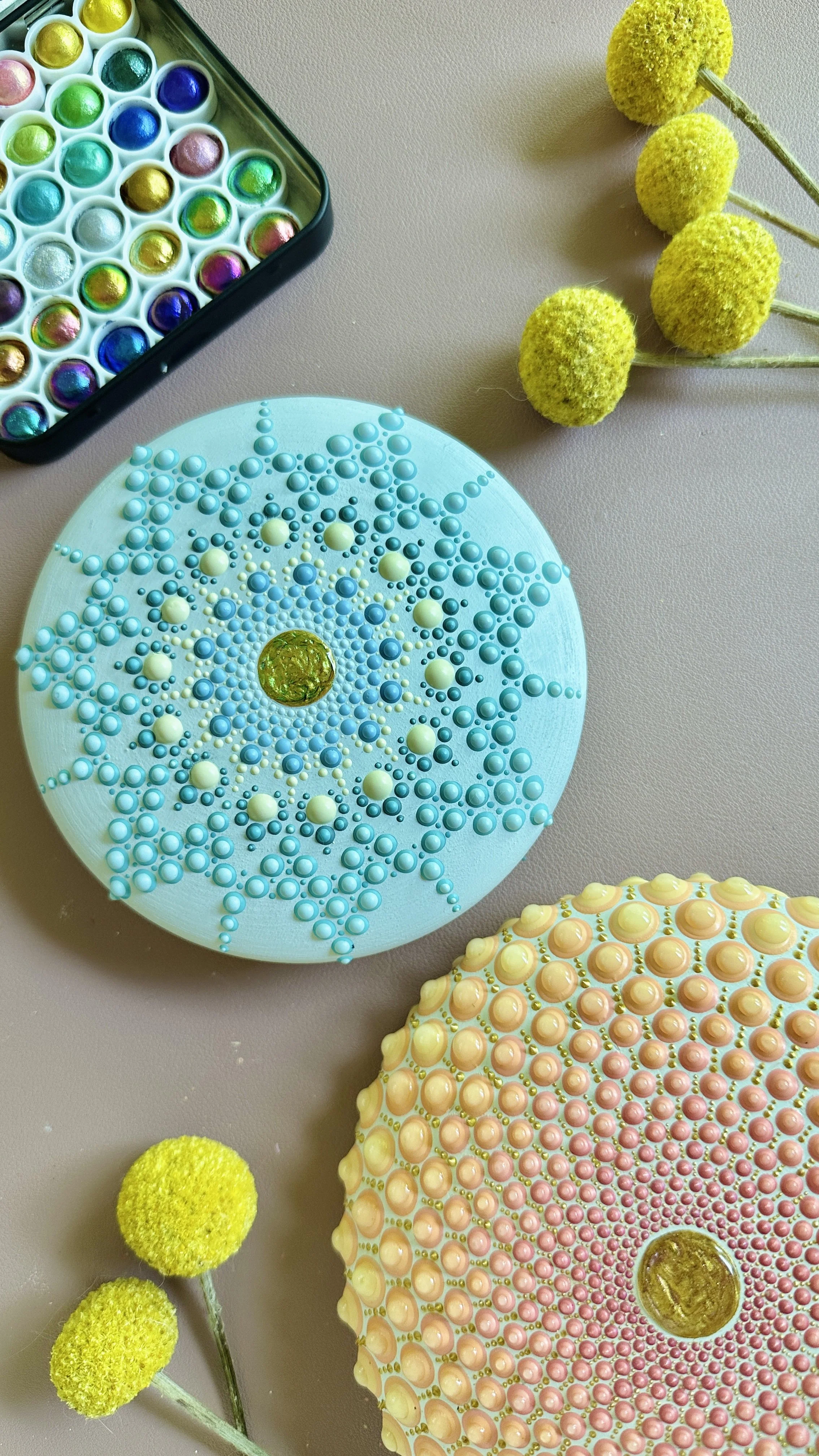 Colorful decorated pastries with intricate dot patterns, yellow and pink, and yellow fluffy billy ball flowers on a beige surface.