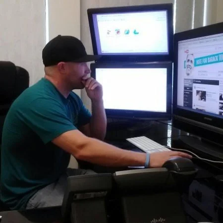 Man in blue shirt sitting at desk looking at two computer screens