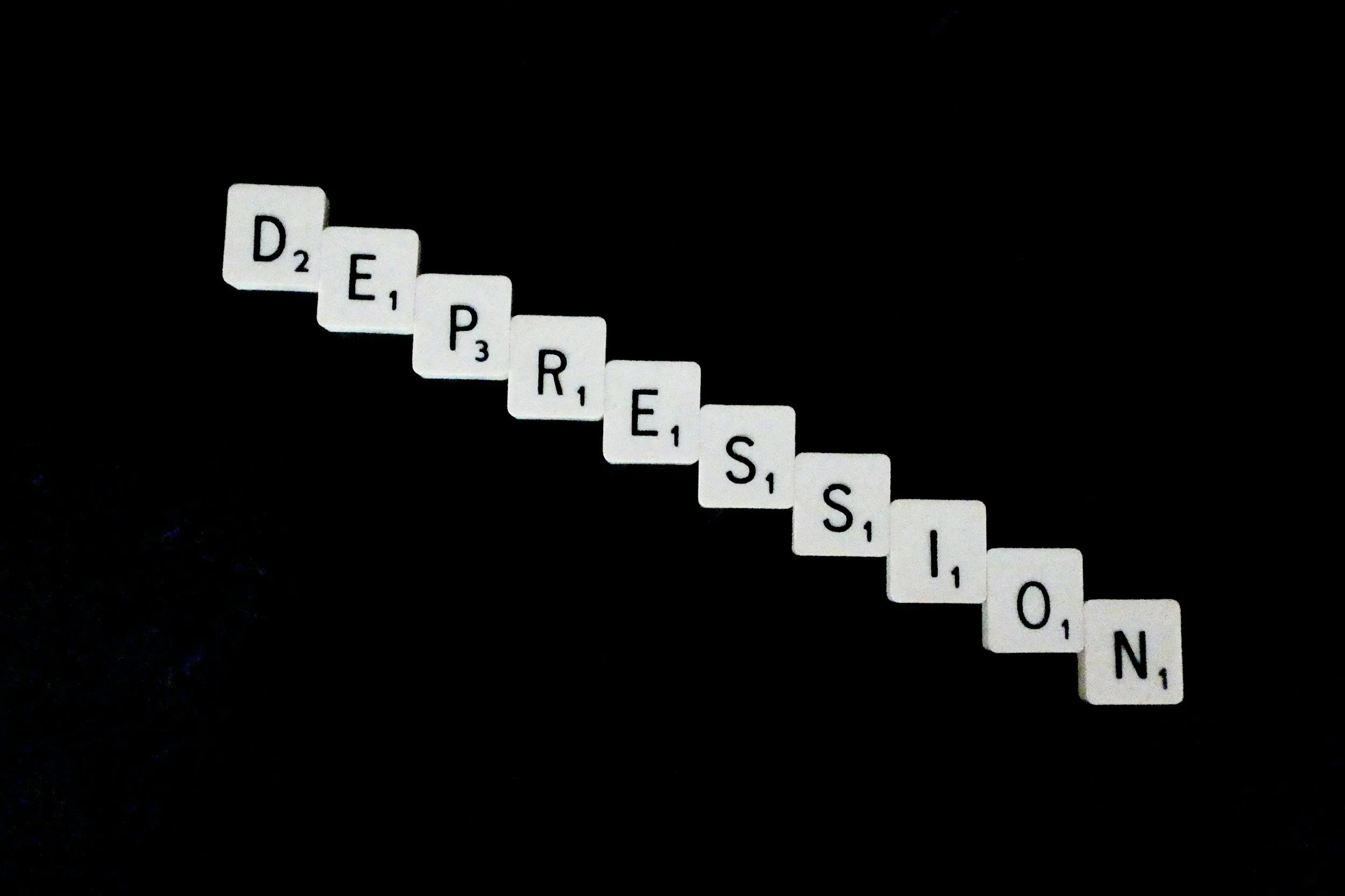 The word depression spelled out in a diagonal using white Scrabble tiles on a black background.