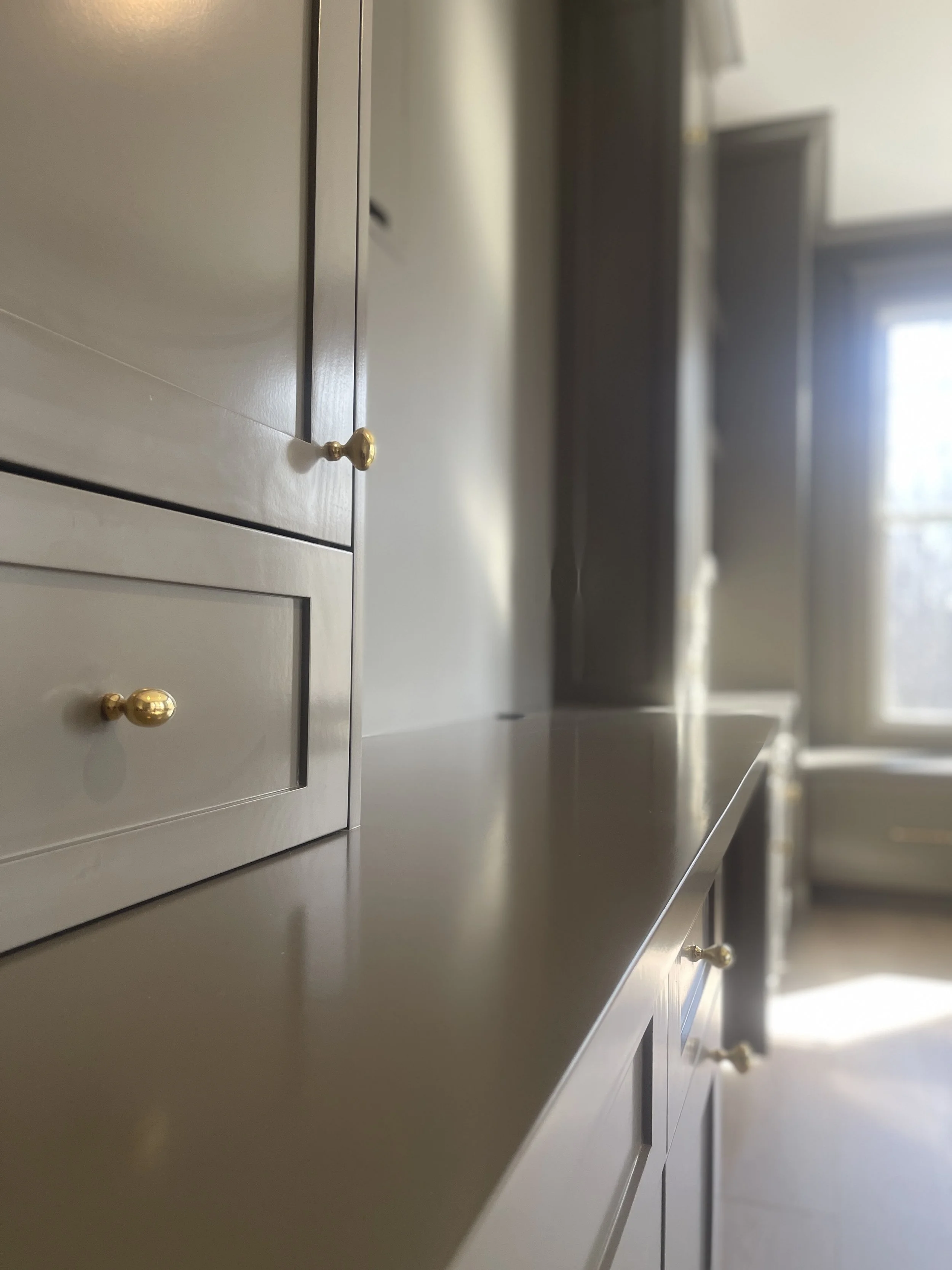 Custom Office and Window Sitting Area with under bench storage.  Color saturated with a moody gray paint with unlacquered brass knobs and pulls.