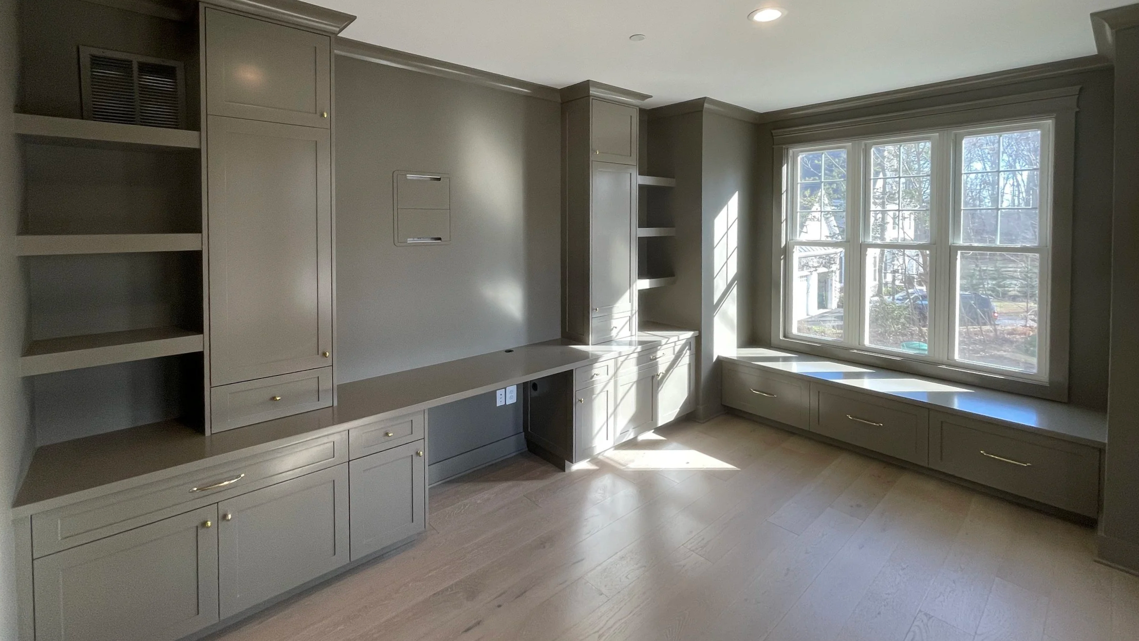 Custom Office and Window Sitting Area with under bench storage.  Color saturated with a moody gray paint with unlacquered brass knobs and pulls.