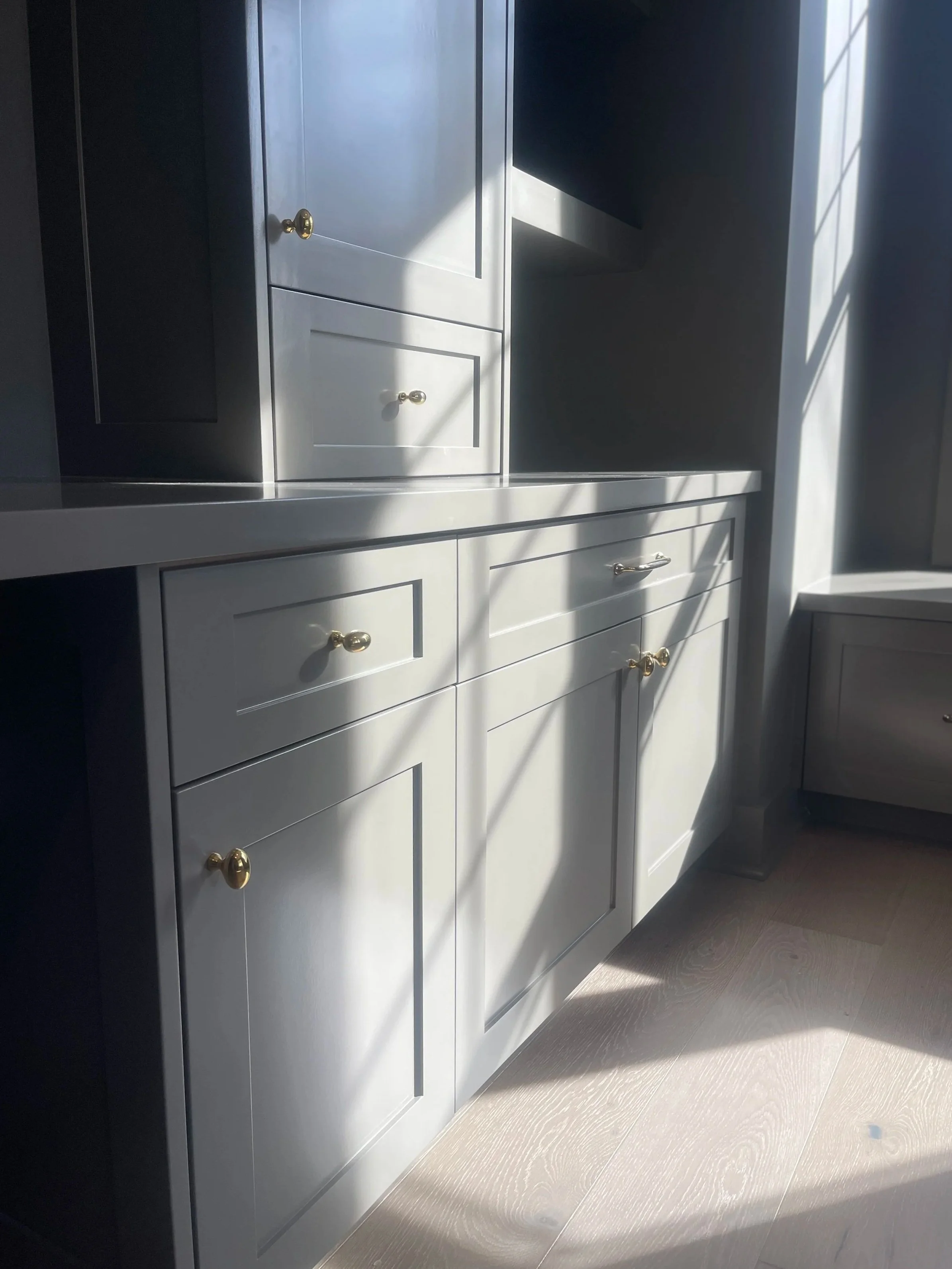 Custom Office and Window Sitting Area with under bench storage.  Color saturated with a moody gray paint with unlacquered brass knobs and pulls.