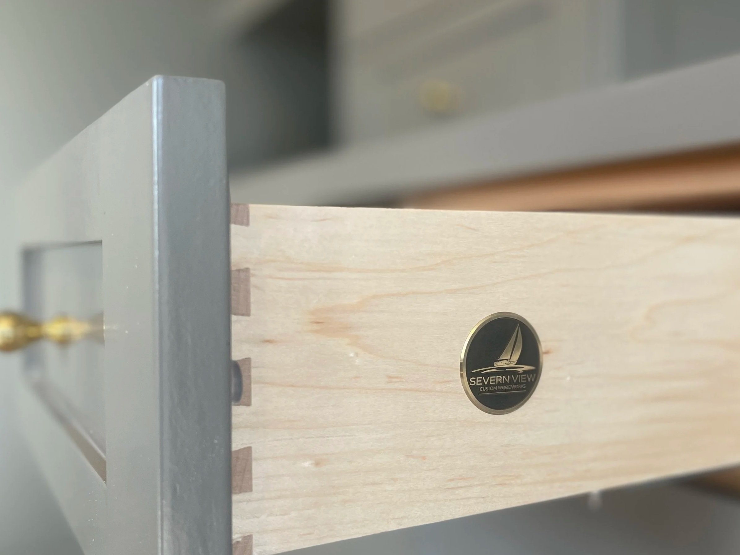 Custom Office and Window Sitting Area with under bench storage.  Color saturated with a moody gray paint with unlacquered brass knobs and pulls.  Severn View Custom Wooworks Brass Medallion