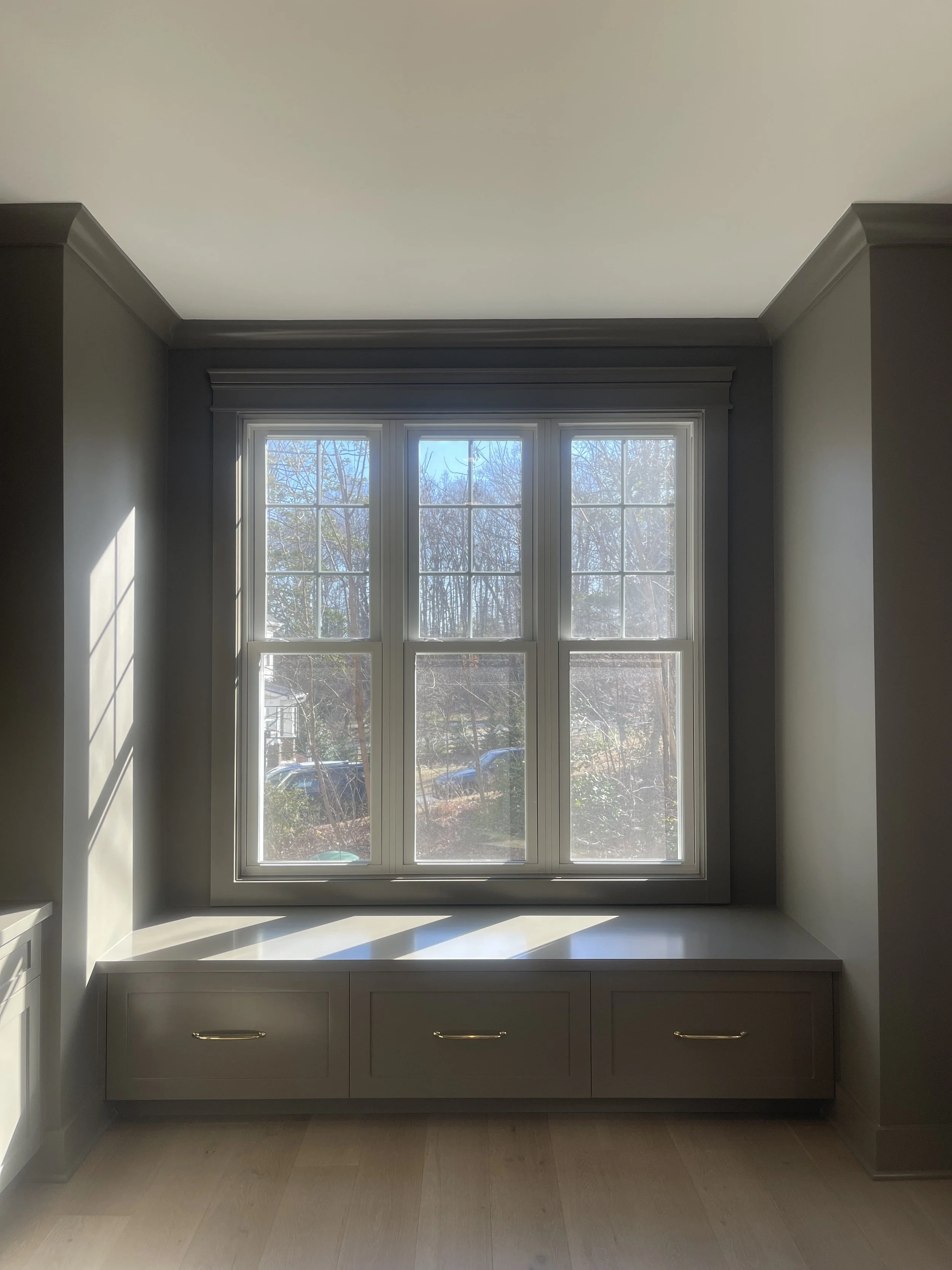 Custom Office and Window Sitting Area with under bench storage.  Color saturated with a moody gray paint with unlacquered brass knobs and pulls.