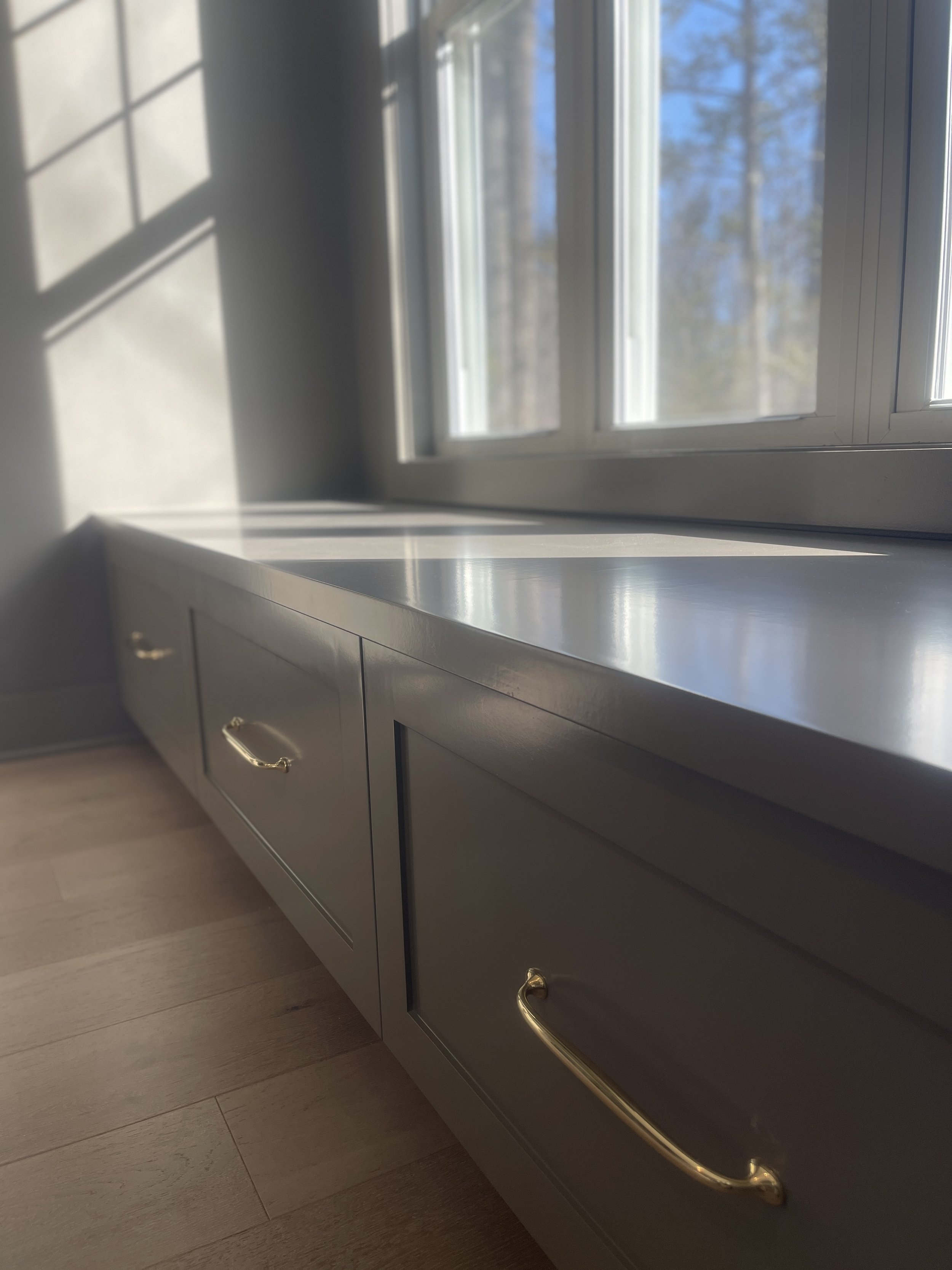 Custom Office and Window Sitting Area with under bench storage.  Color saturated with a moody gray paint with unlacquered brass knobs and pulls.
