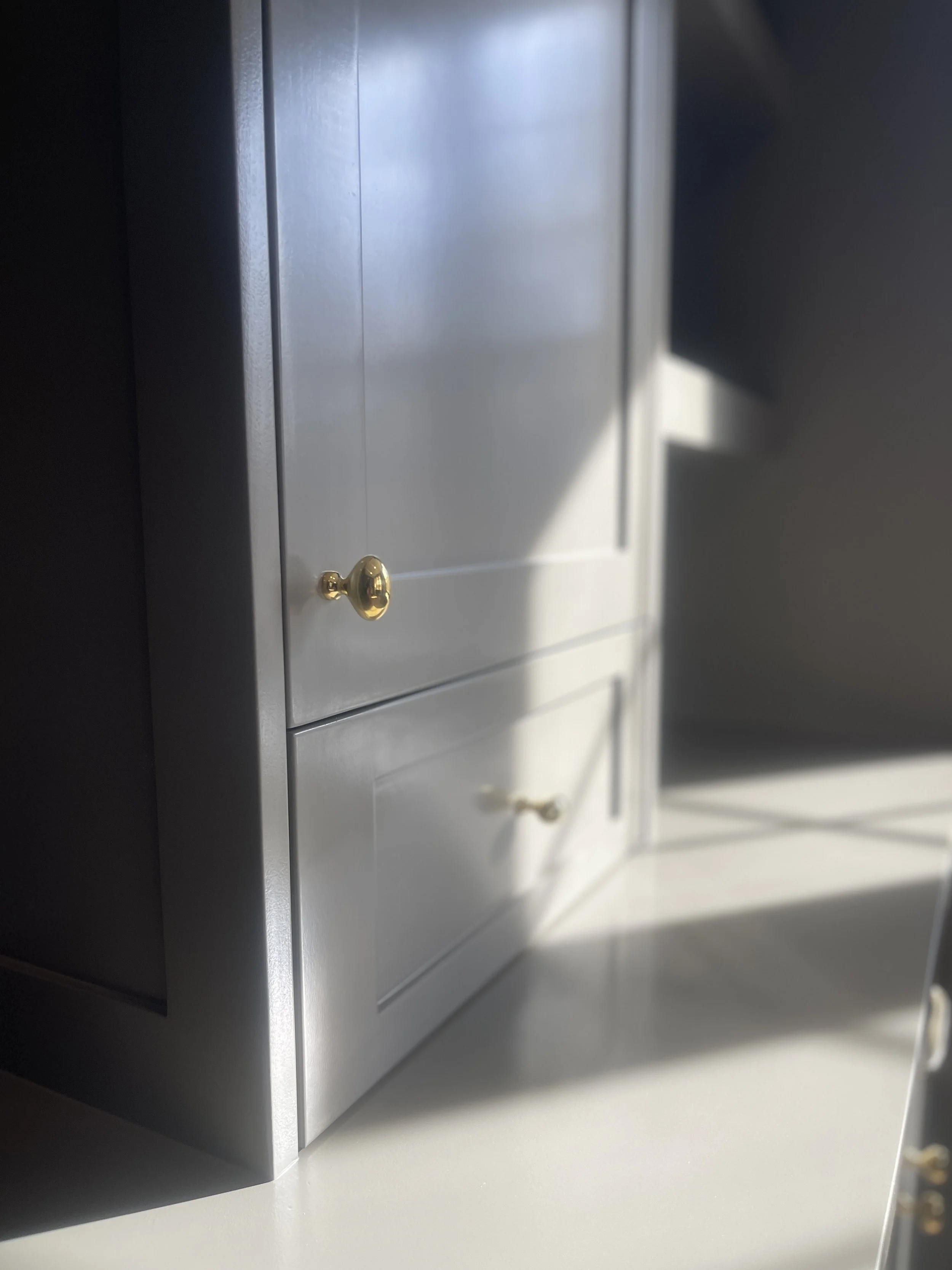 Custom Office and Window Sitting Area with under bench storage.  Color saturated with a moody gray paint with unlacquered brass knobs and pulls.