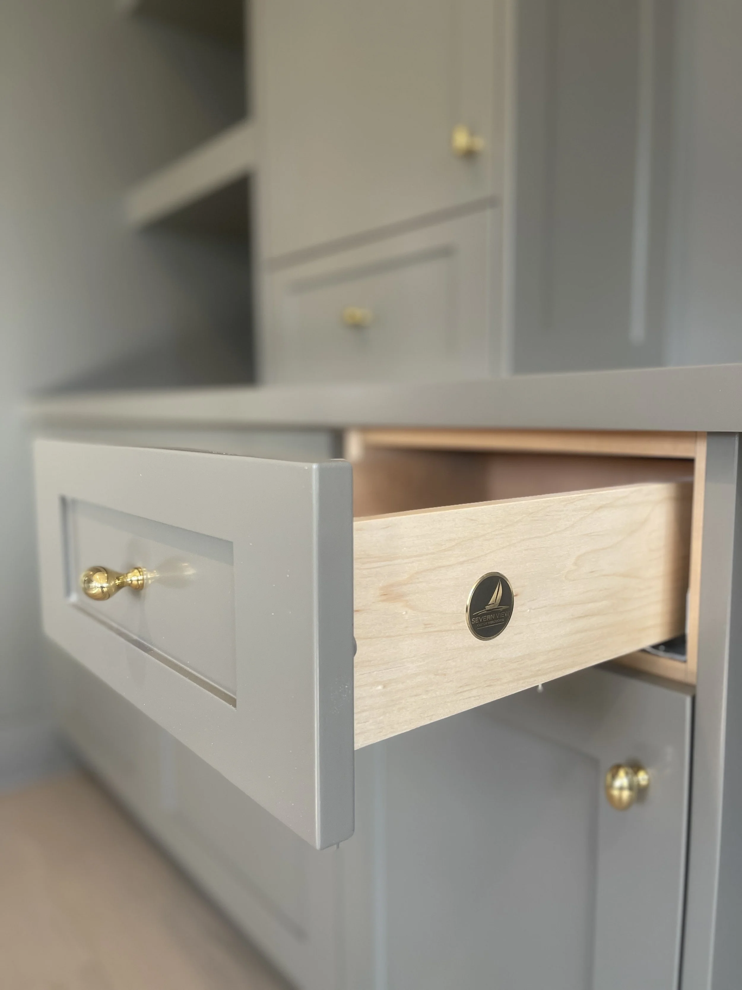 Custom Office and Window Sitting Area with under bench storage.  Color saturated with a moody gray paint with unlacquered brass knobs and pulls.  Severn View Custom Wooworks Brass Medallion