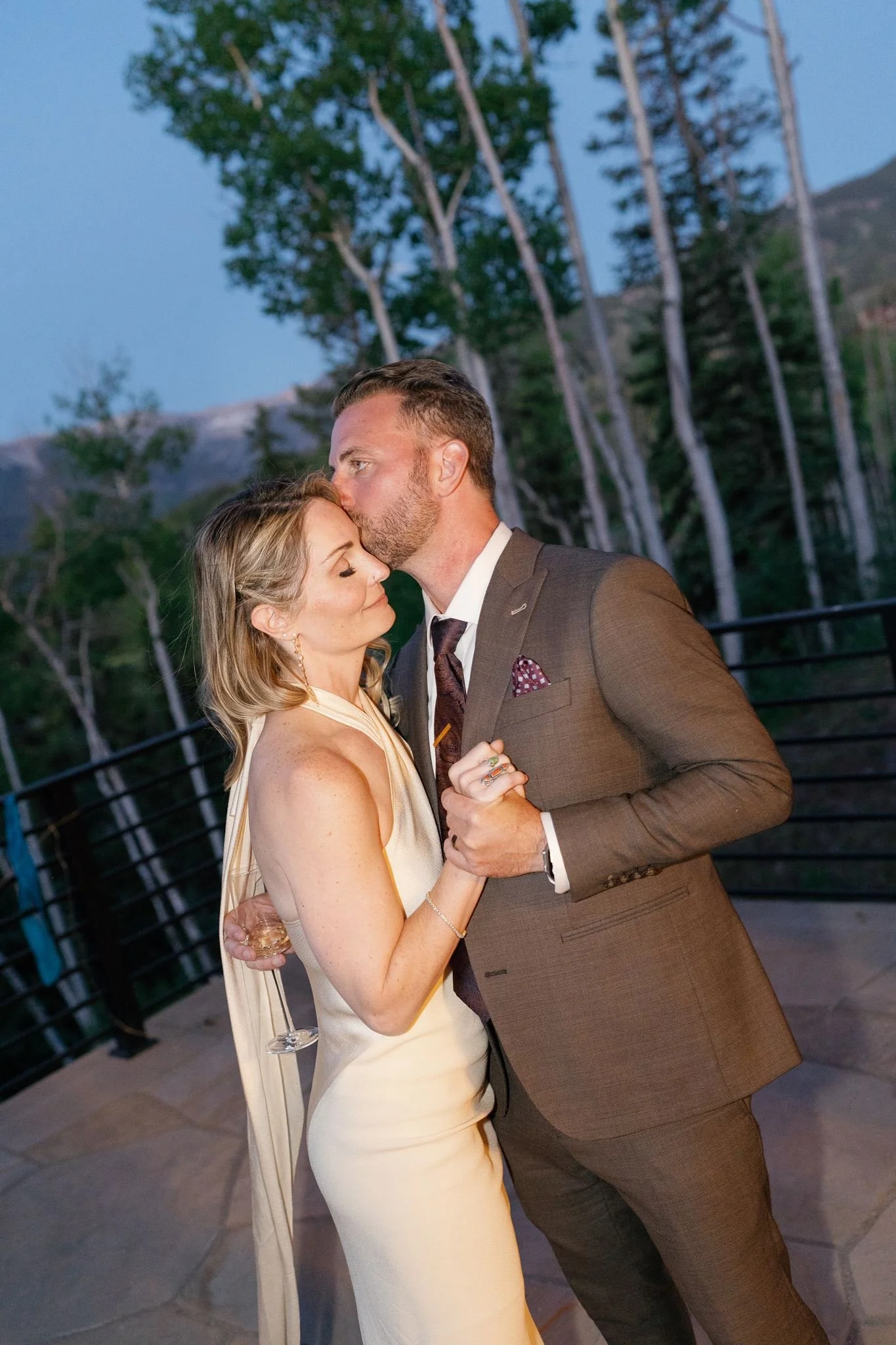groom kisses the bride on the temple as the sun sets
