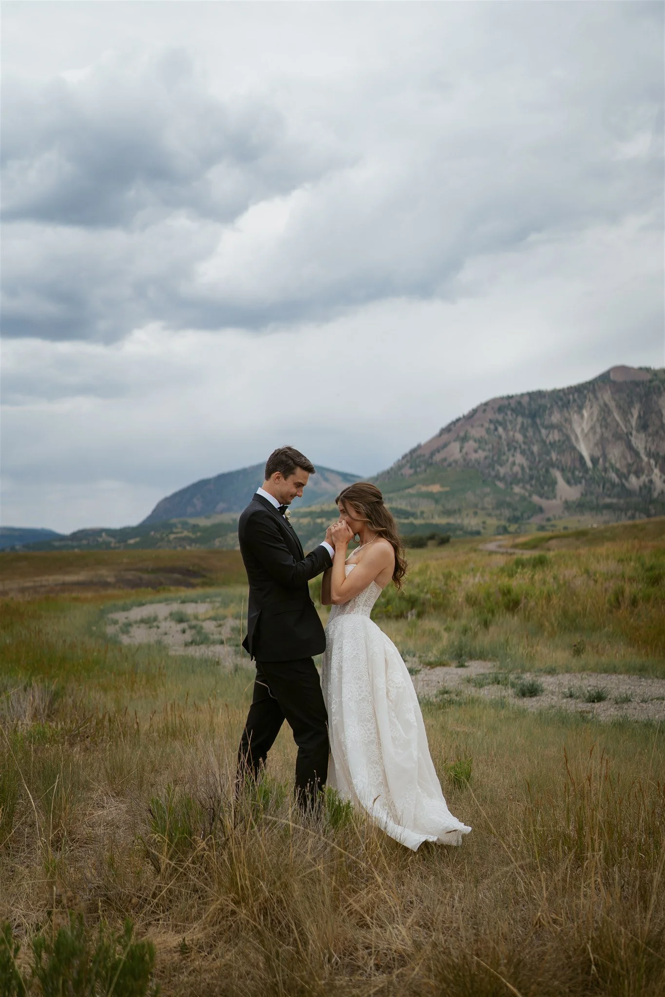groom admiring the bride's dress while she kisses his hands