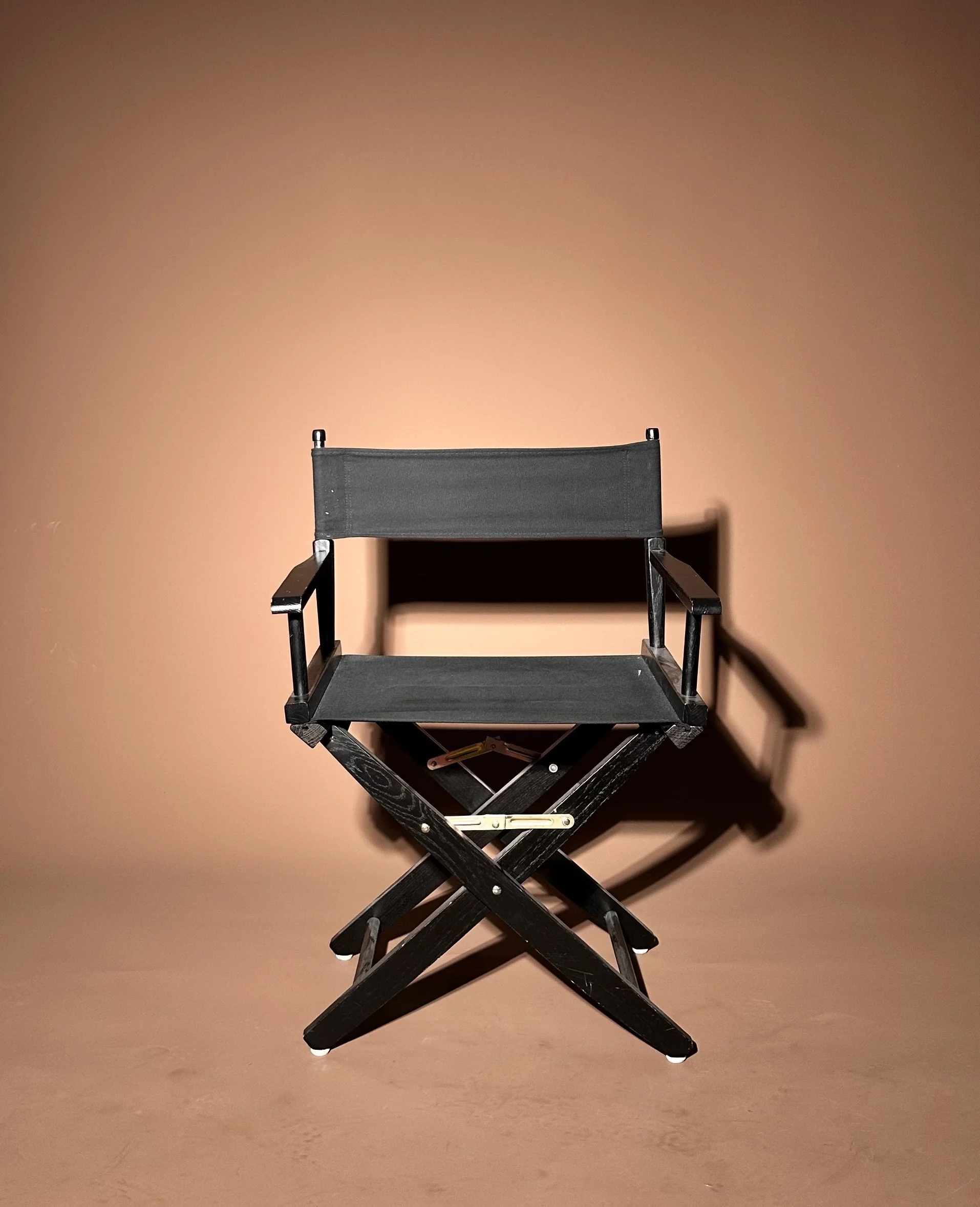 A black folding director's chair against a peach-colored wall with shadows cast to the right at a photography studio in San Antonio, Texas.