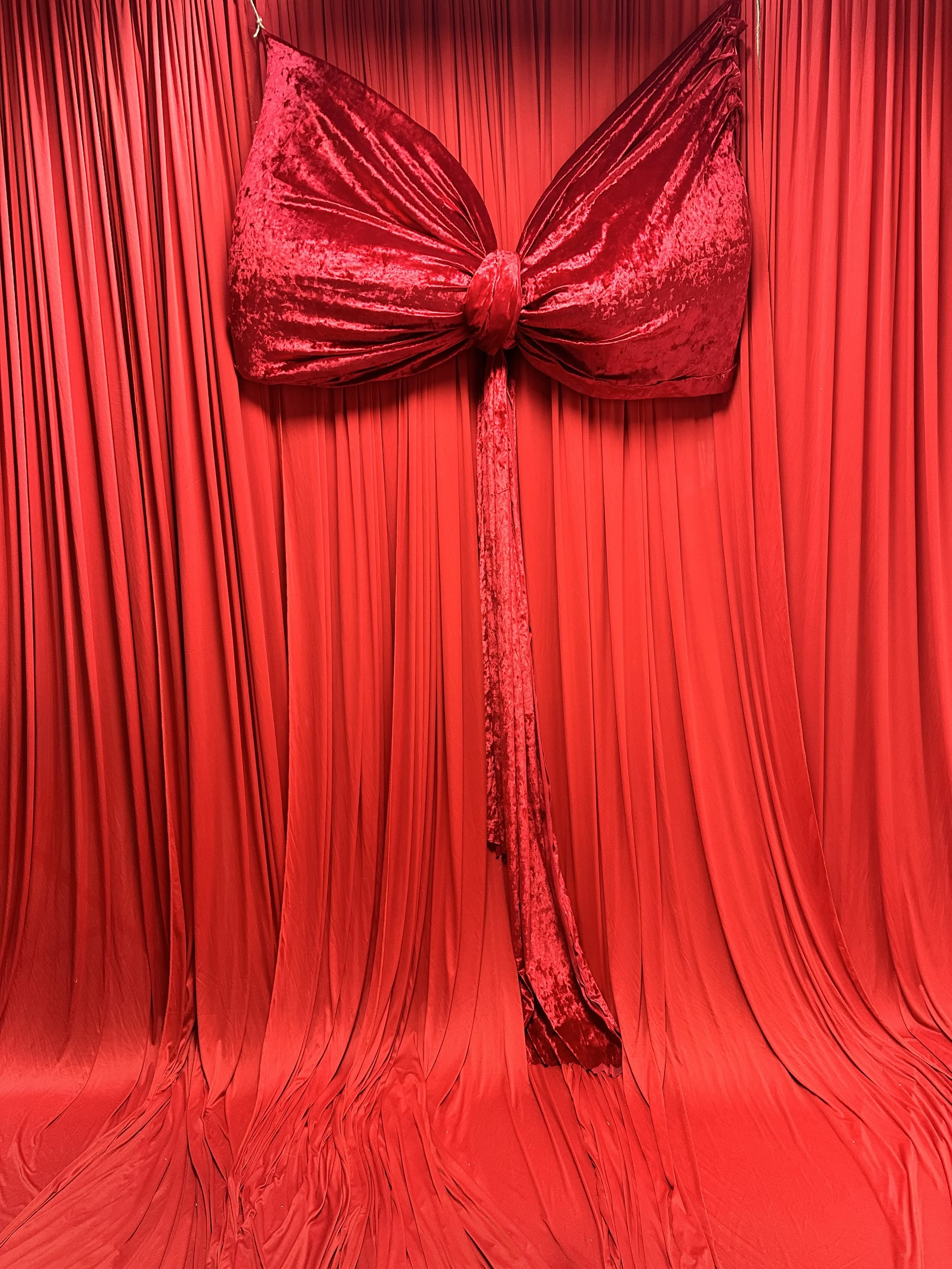 A red velvet bow tied on a red pleated curtain backdrop for Christmas minis in San Antonio, Texas.