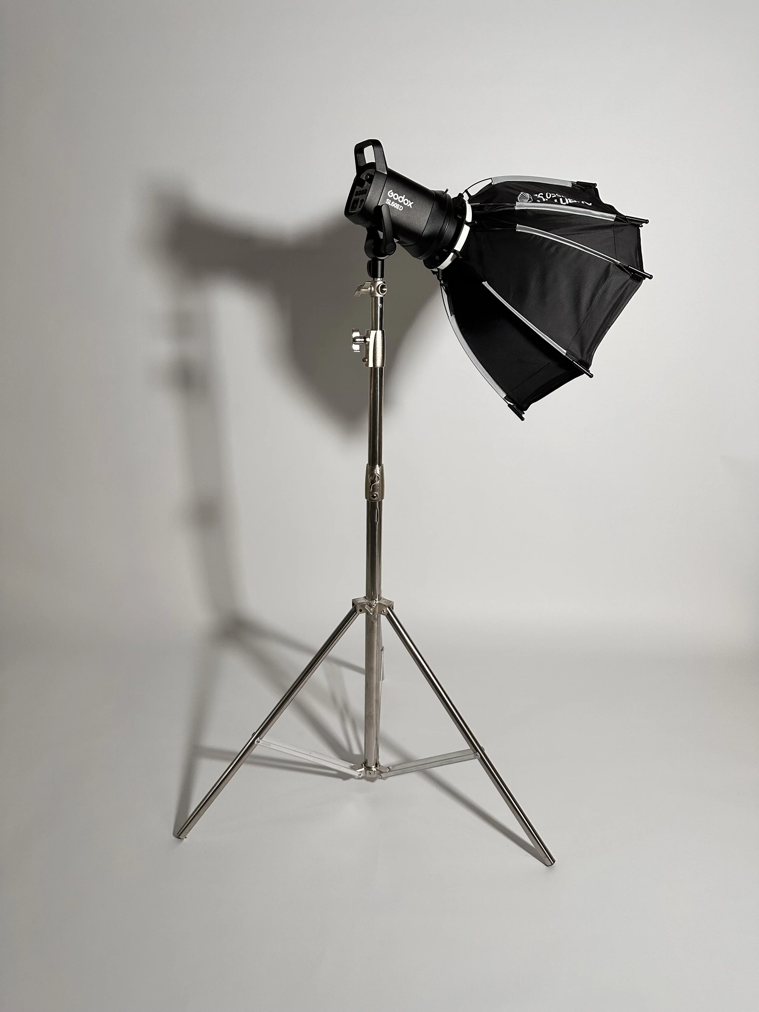 A studio light with a black umbrella reflector on a metal stand against a plain white background.