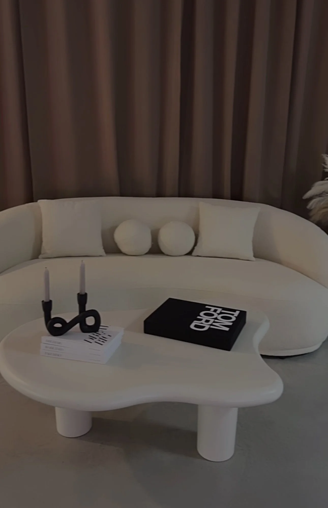 Modern living room with a white curved sofa, a white coffee table, neutral curtains, and decorative pillows.