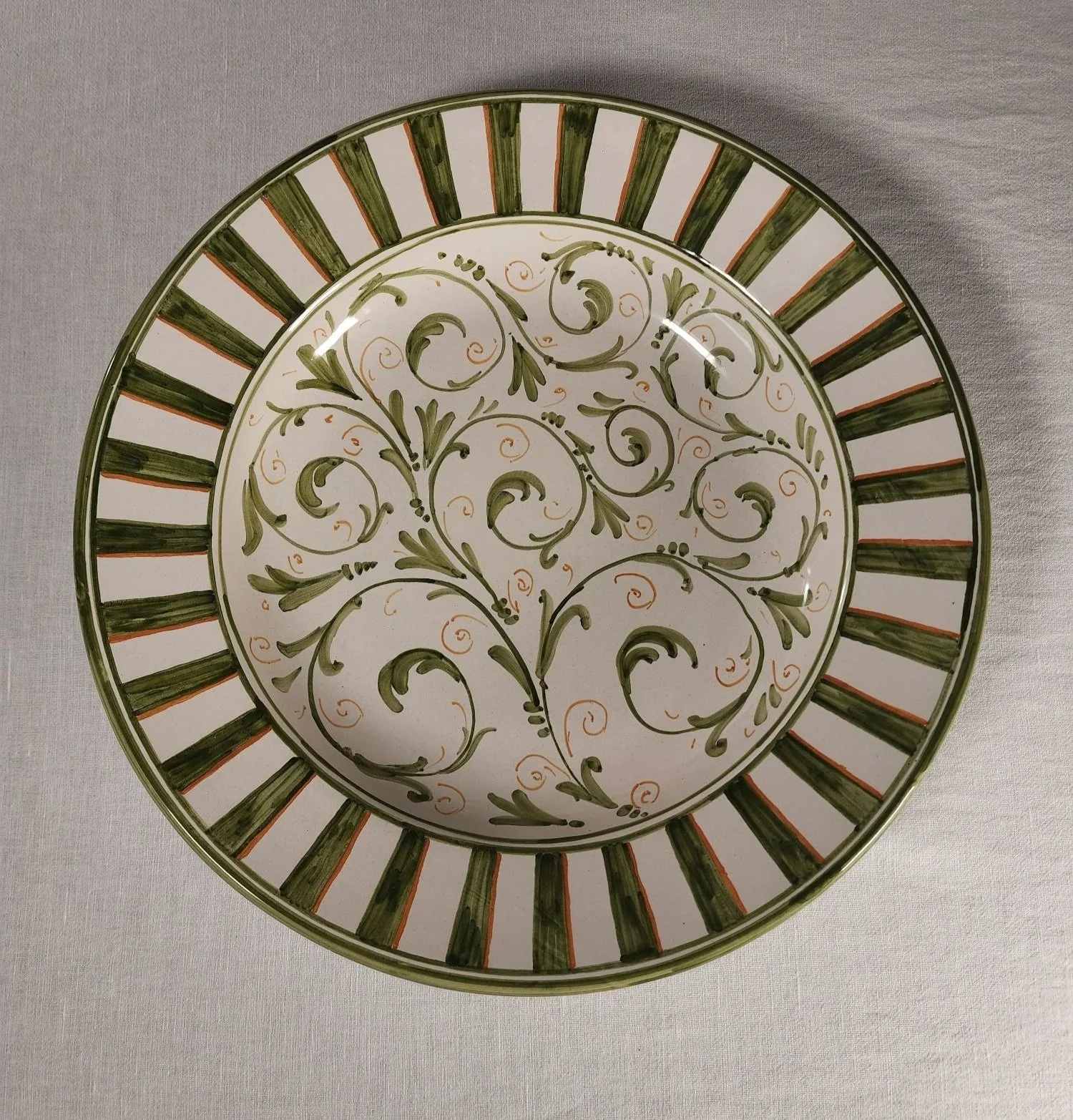 Decorative ceramic plate with green and orange floral patterns and concentric green and orange striped border.