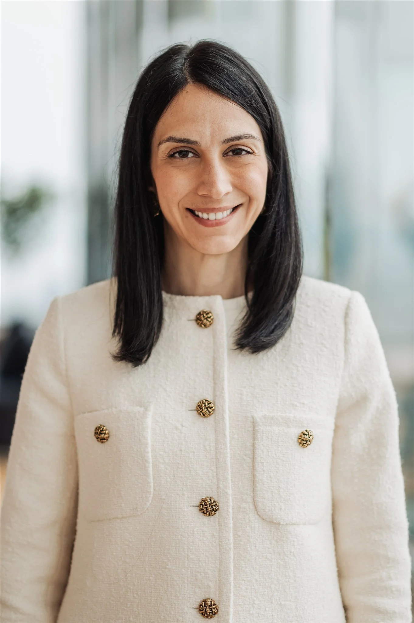 Corporate headshot of a smiling woman in a cream tweed jacket by a bright window, Montreal