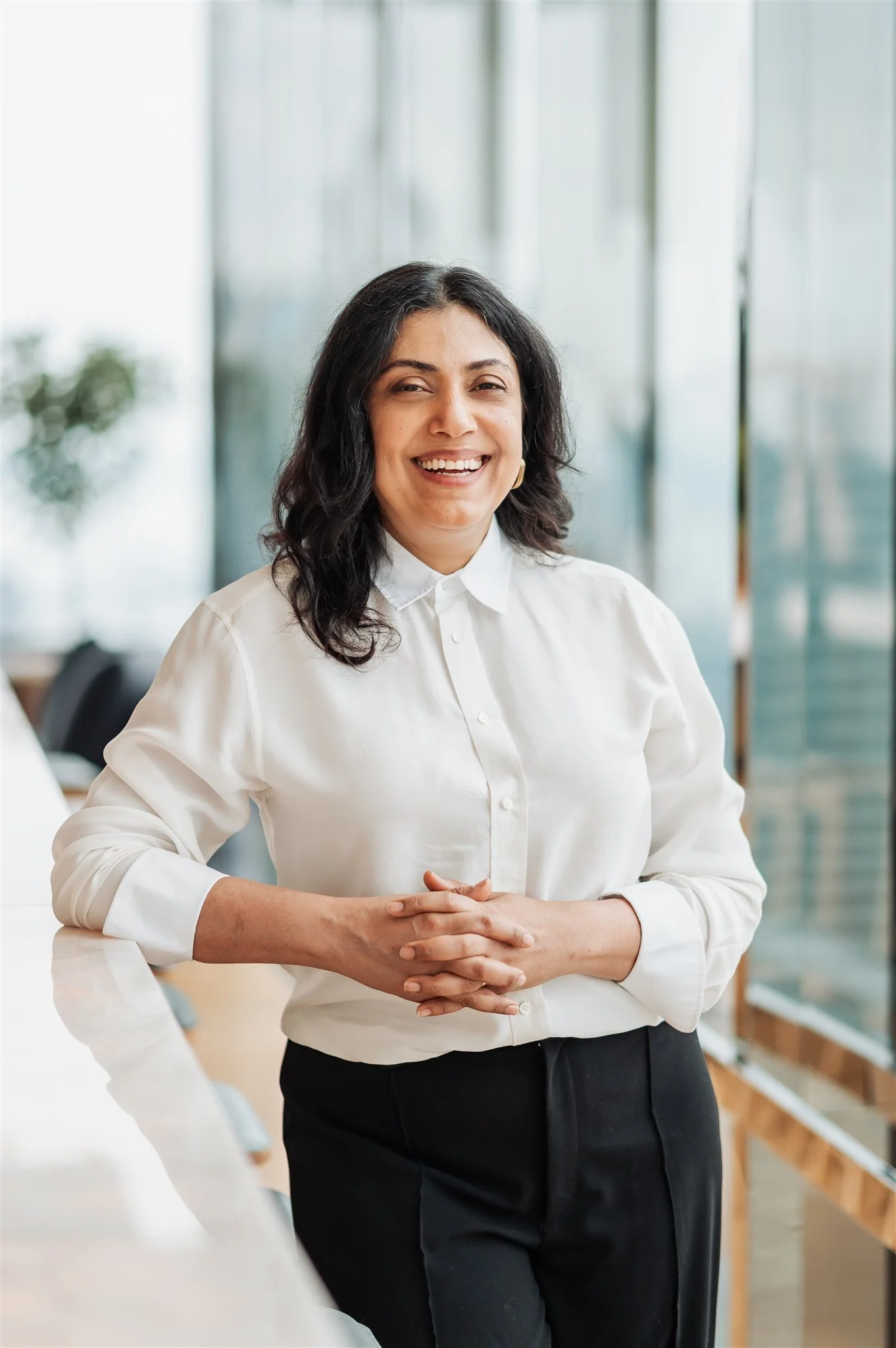 Corporate portrait of a woman with dark curly hair in a white shirt by a glass wall, Montreal