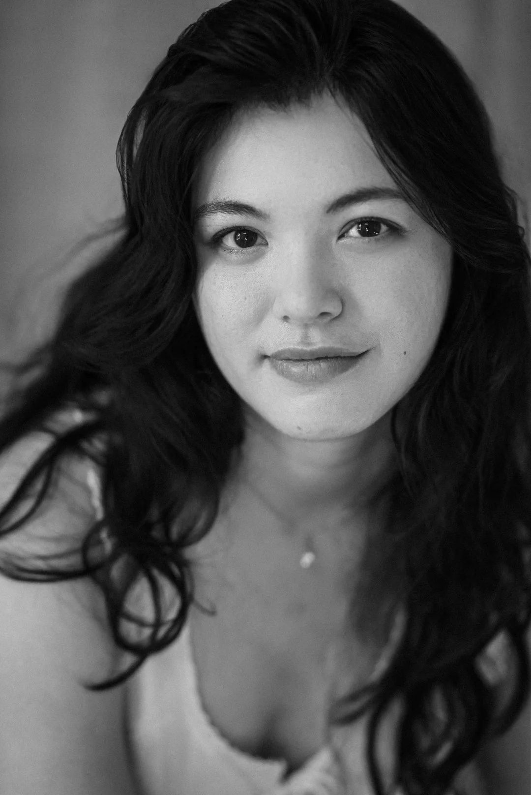 Black and white actor headshot of a woman with long tousled dark hair and a soft smile, Montreal
