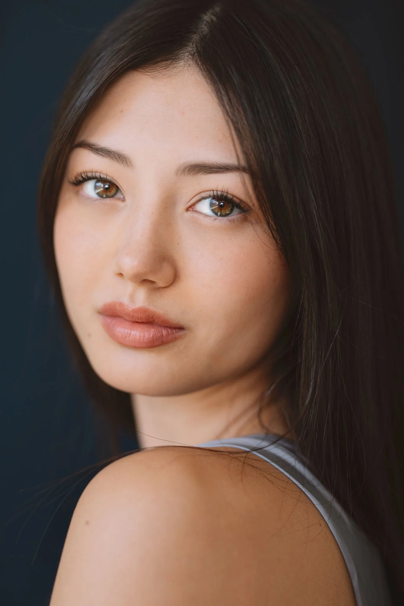 Close-up actor headshot of a woman with long dark hair glancing over her shoulder, navy backdrop, Montreal
