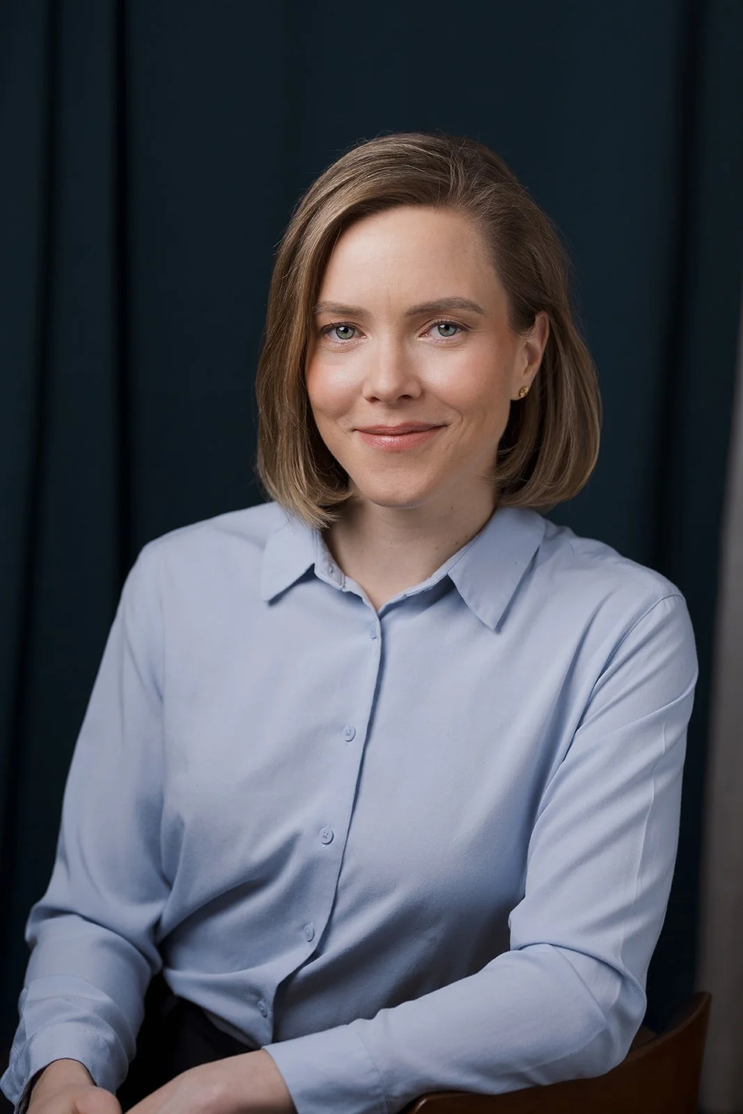 Woman with shoulder-length light brown hair, light blue button shirt, dark backdrop - actor headshot by Tea & Oranges, Montreal portrait photographer