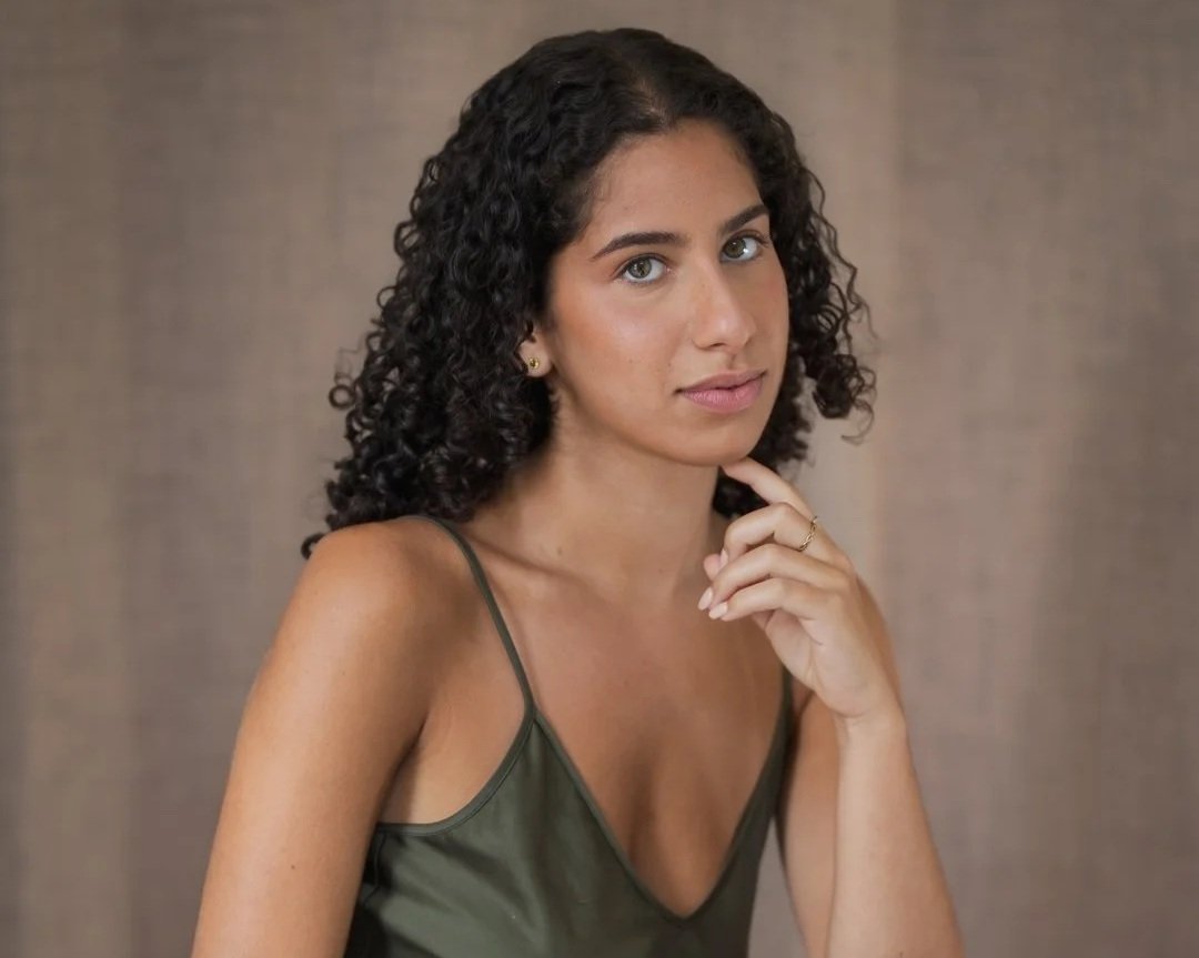 Woman with dark curly hair, hand at her chin, olive tank top, taupe backdrop - actor headshot by Tea & Oranges, Montreal portrait photographer