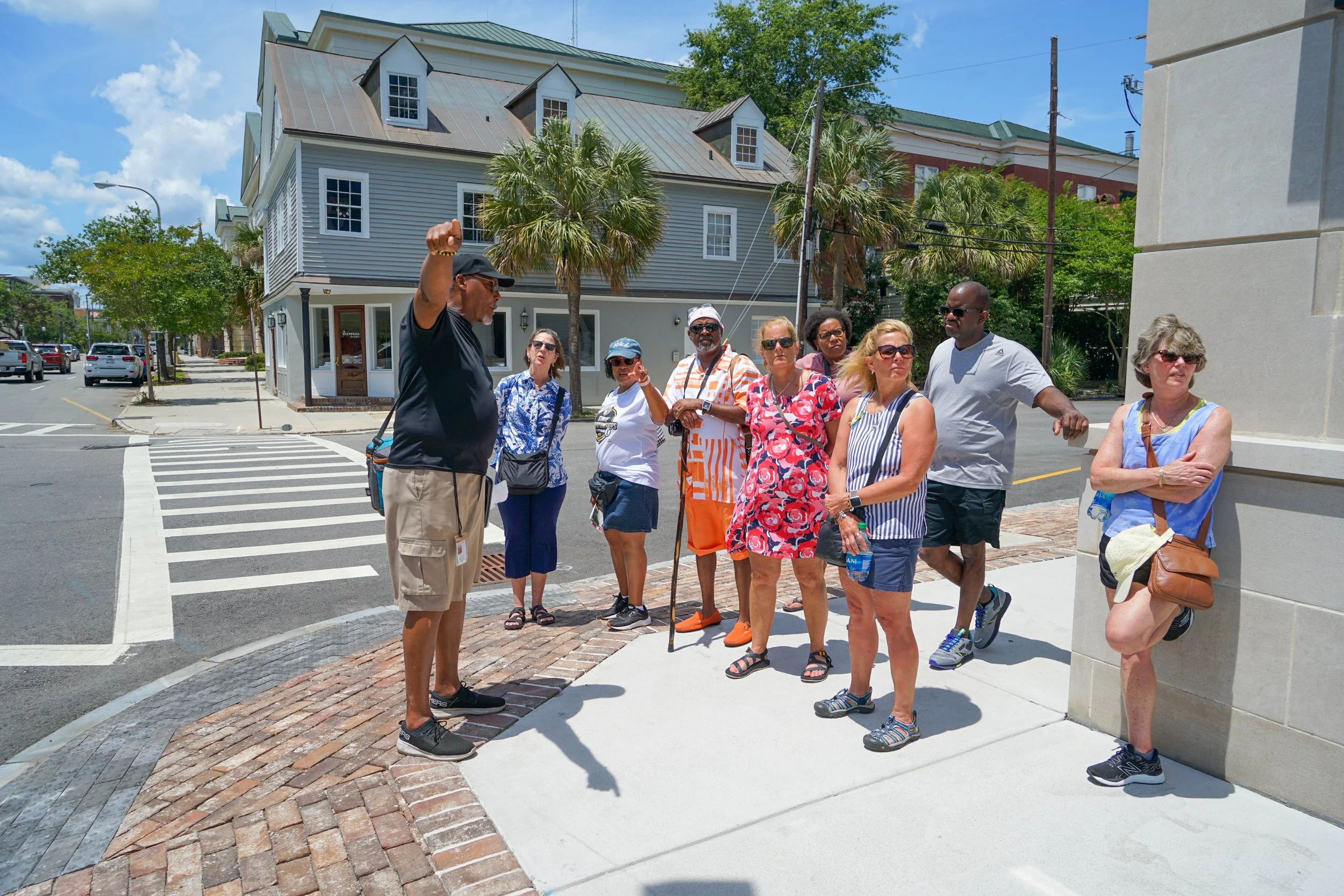 Tour group listening to a guide on a city street with colorful buildings, palm trees, and parked cars.