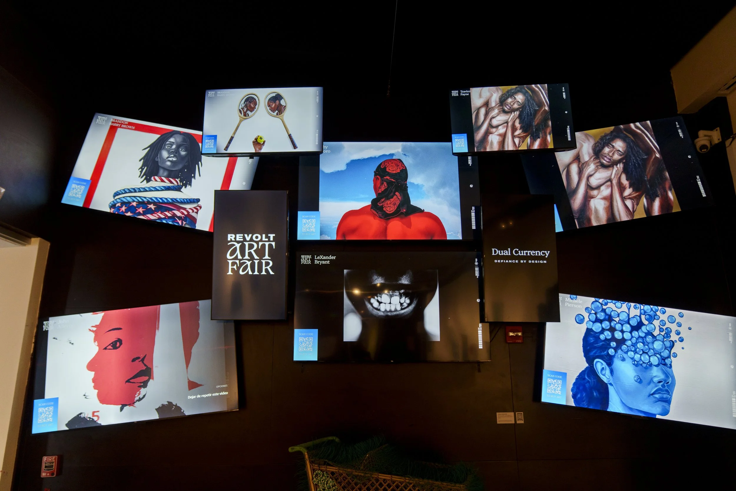 Multiple digital screens displaying various artworks and advertisements at an art fair, with some screens showing portraits, abstract designs, and promotional text.