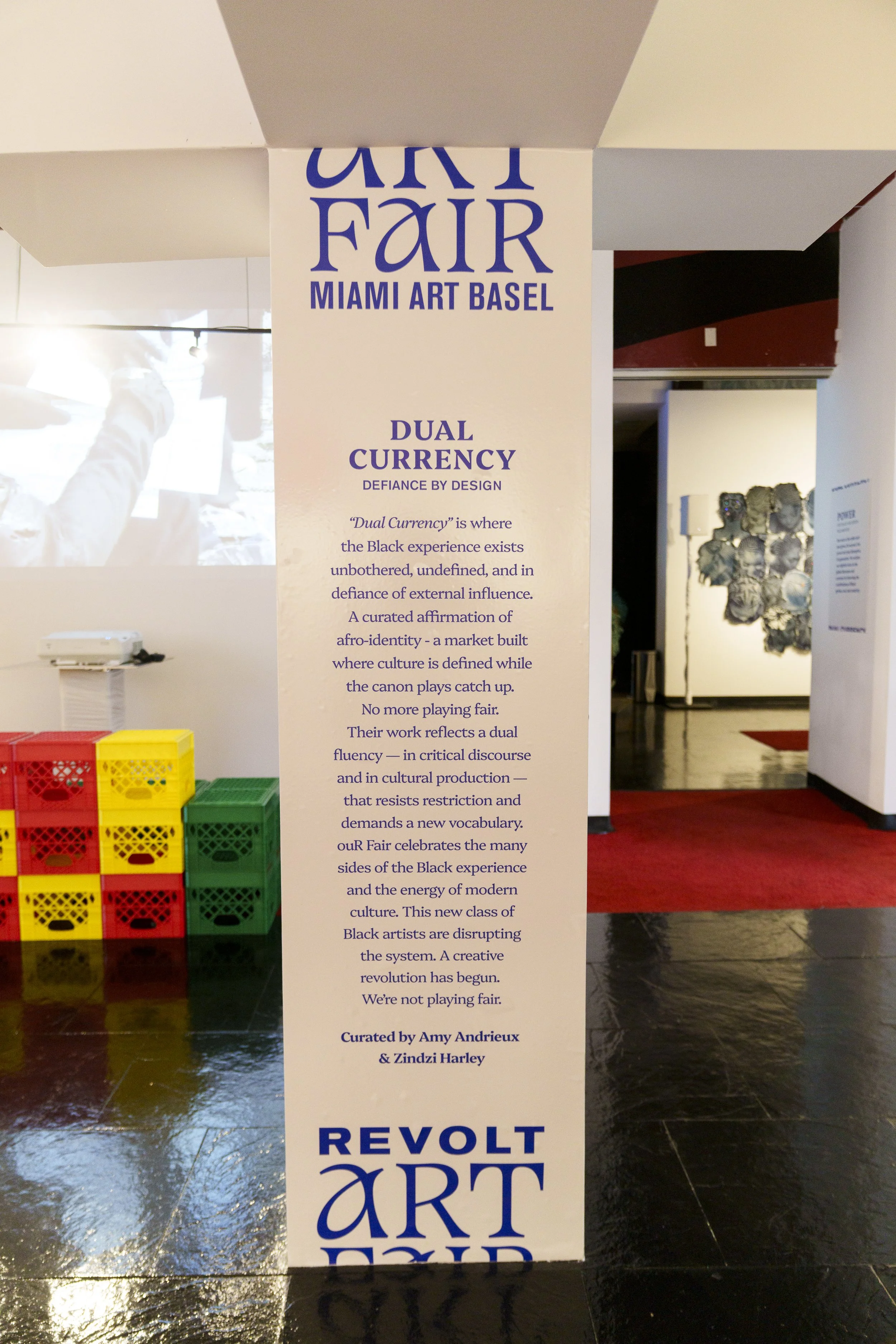 Exhibition panel for Miami Art Basel titled 'Dual Currency' with descriptive text about Black cultural experience and a display of colorful crates on the left side.
