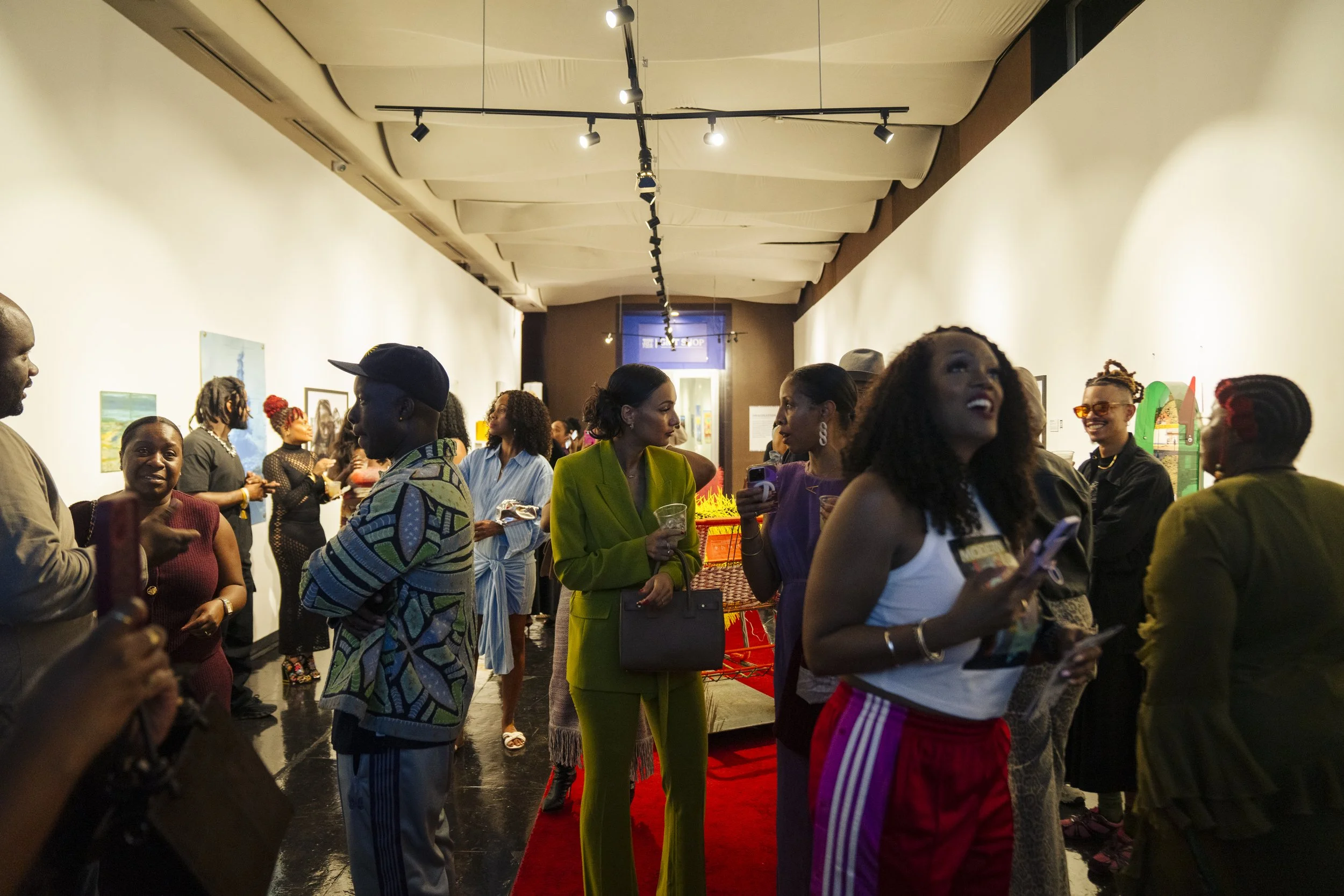 People socializing at an art gallery, various artworks on the walls, group conversations, and some attendees holding drinks.
