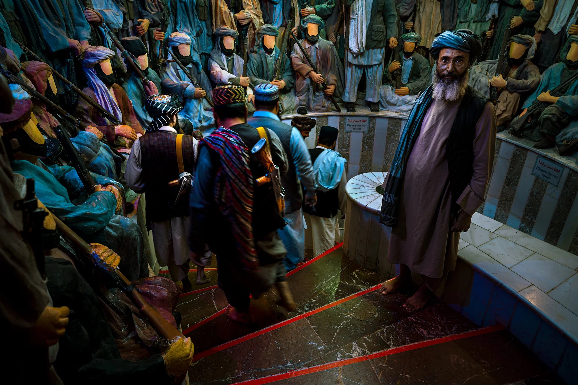 A former mujahideen, now a museum guard, lets armed Taliban pass. Around him, statues stand with the erased faces of the mujahideen who liberated the country from the invasion. The museum becomes a conflict between a denied past authority and a prese