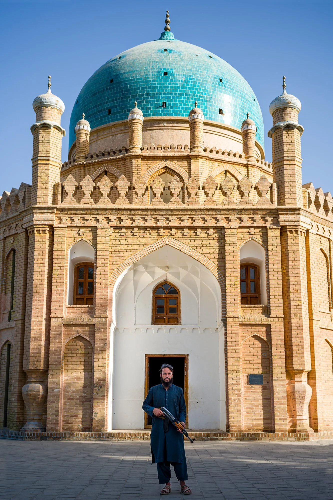 At dawn, in front of the Mausoleum of Mirwais Hotak, a young, armed Taliban man stands proudly and solemnly vigil over this extraordinary sacred site. Dedicated to the celebrated Afghan leader, the mausoleum is a space of devotion, remembrance, and r