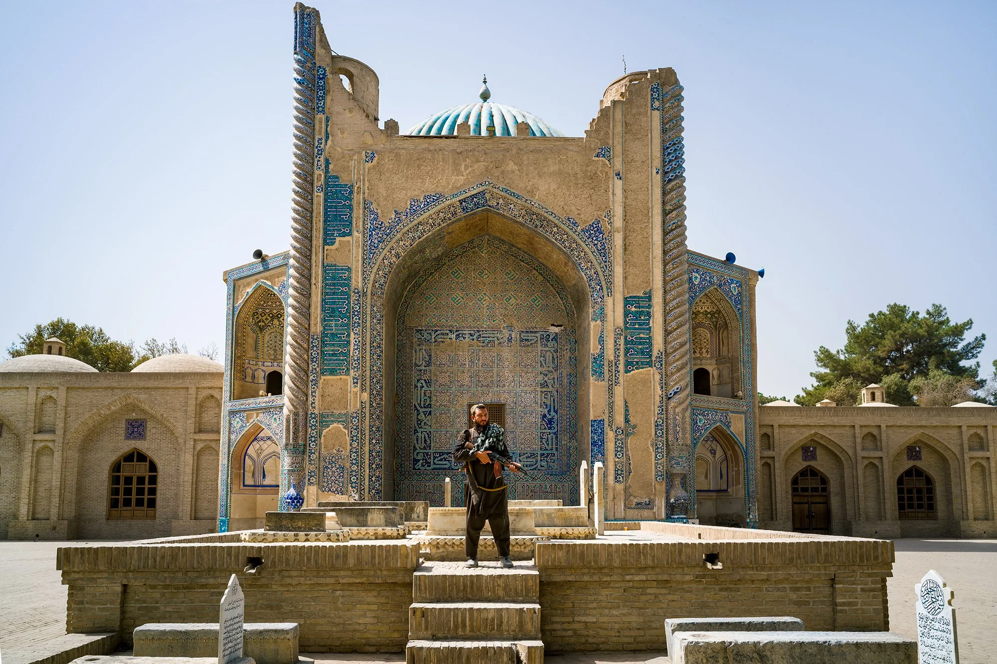 In front of the Green Mosque in Balkh, a sacred site and the spiritual heart of northern Afghanistan, an armed Taliban stands vigil among the ancient tombs of the faithful. Its presence, a symbol of protection and power, reflects the profound and com