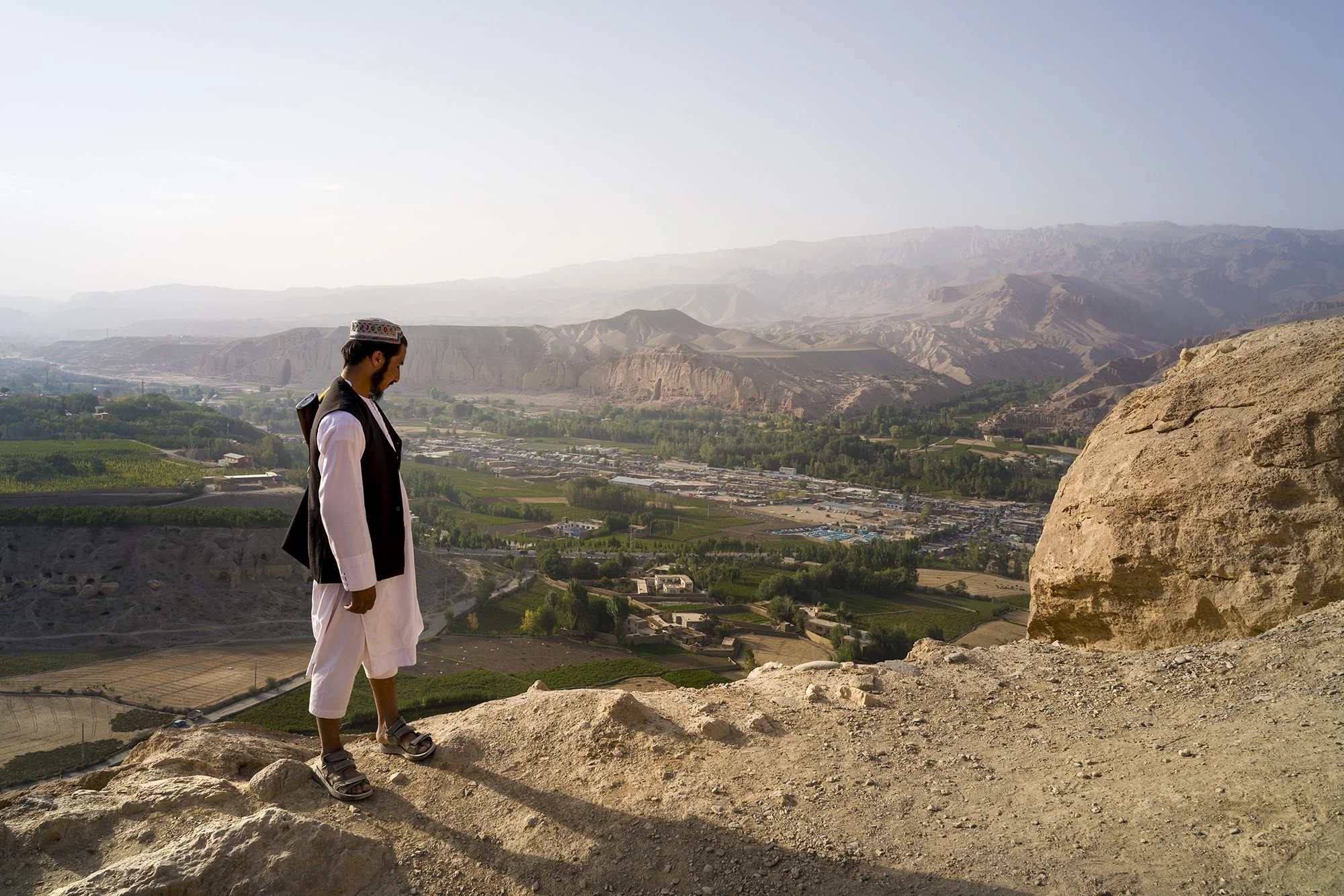 At the edge of the 11th-century fortress of Shahr-e Gholghola, literally "City of Screams," an armed Taliban guard watches over the valley and the path leading to the summit. The ruins overlook the Bamiyan Valley, with the spires in the distance wher