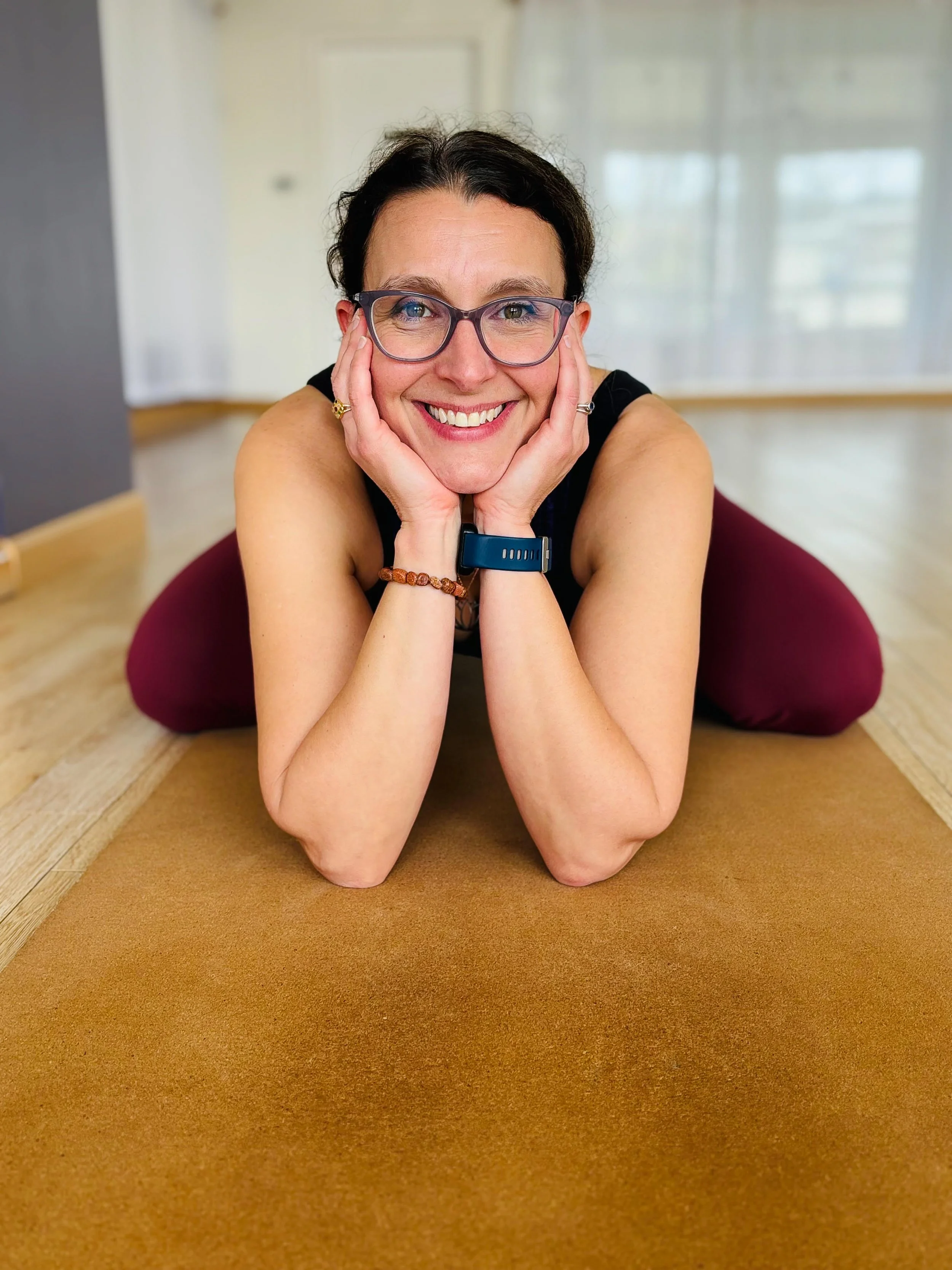 Woman practicing yoga on her stomach on a yoga mat indoors, smiling and looking at the camera.