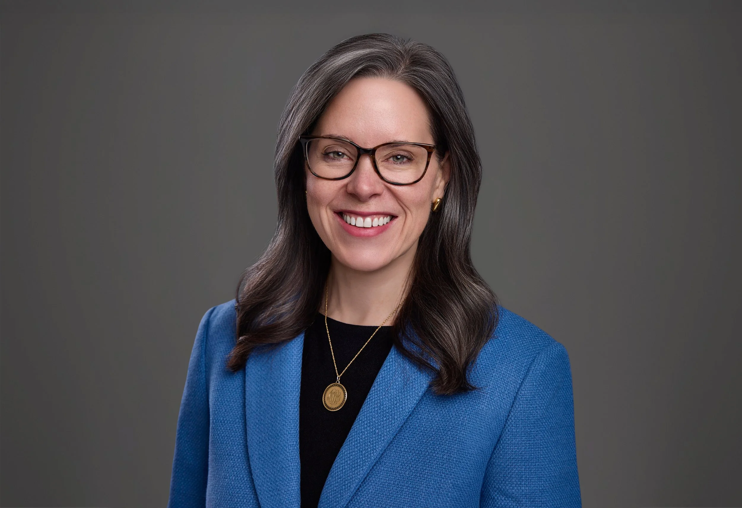 Law firm headshot of a smiling Thompson Burton professional in glasses and a blue blazer, matching gray background for a unified team look, by Tausha Dickinson Photography in Franklin, TN