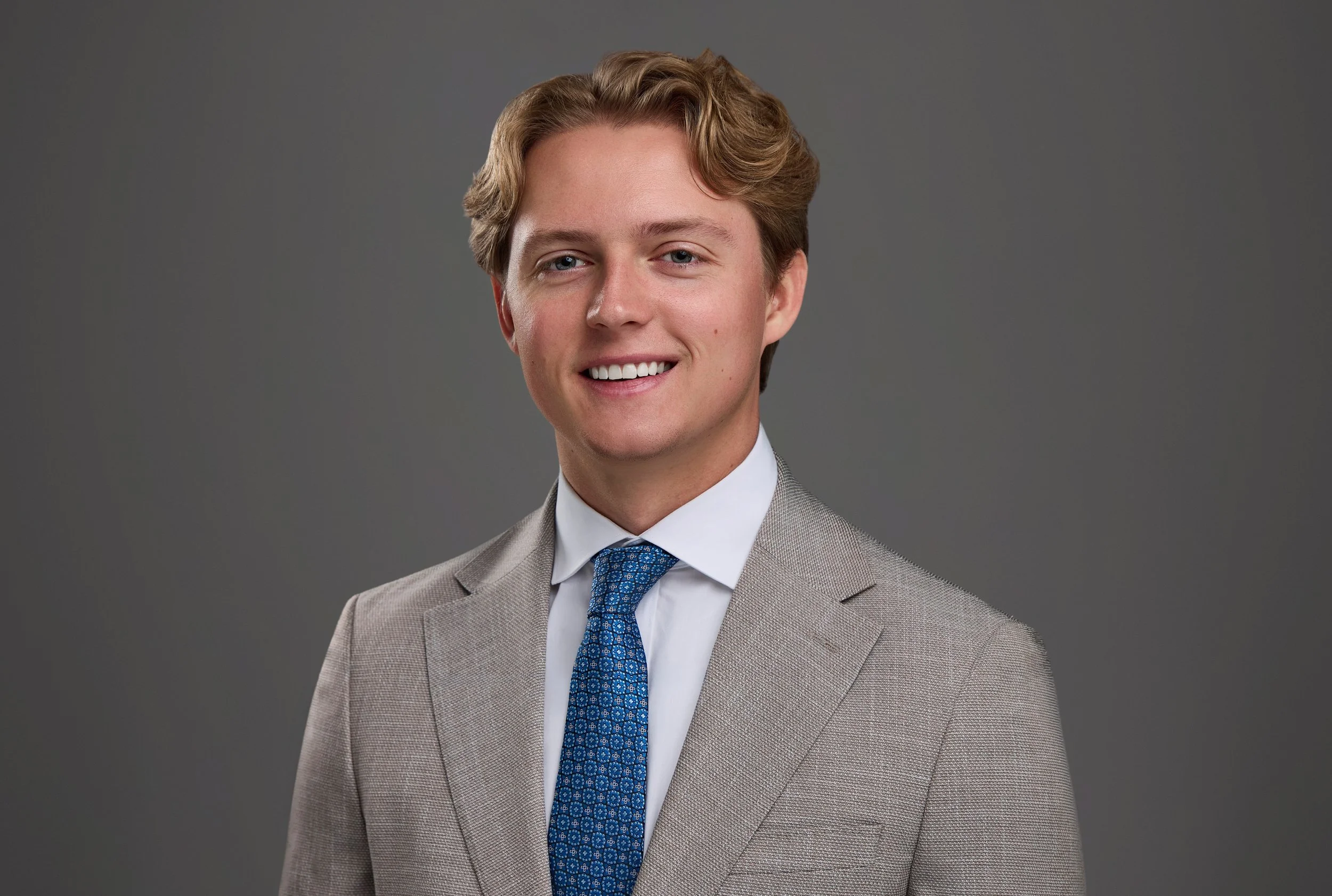 Thompson Burton team headshot of a smiling professional in a tan suit and blue patterned tie on a charcoal gray backdrop, photographed by Tausha Dickinson in Franklin, TN
