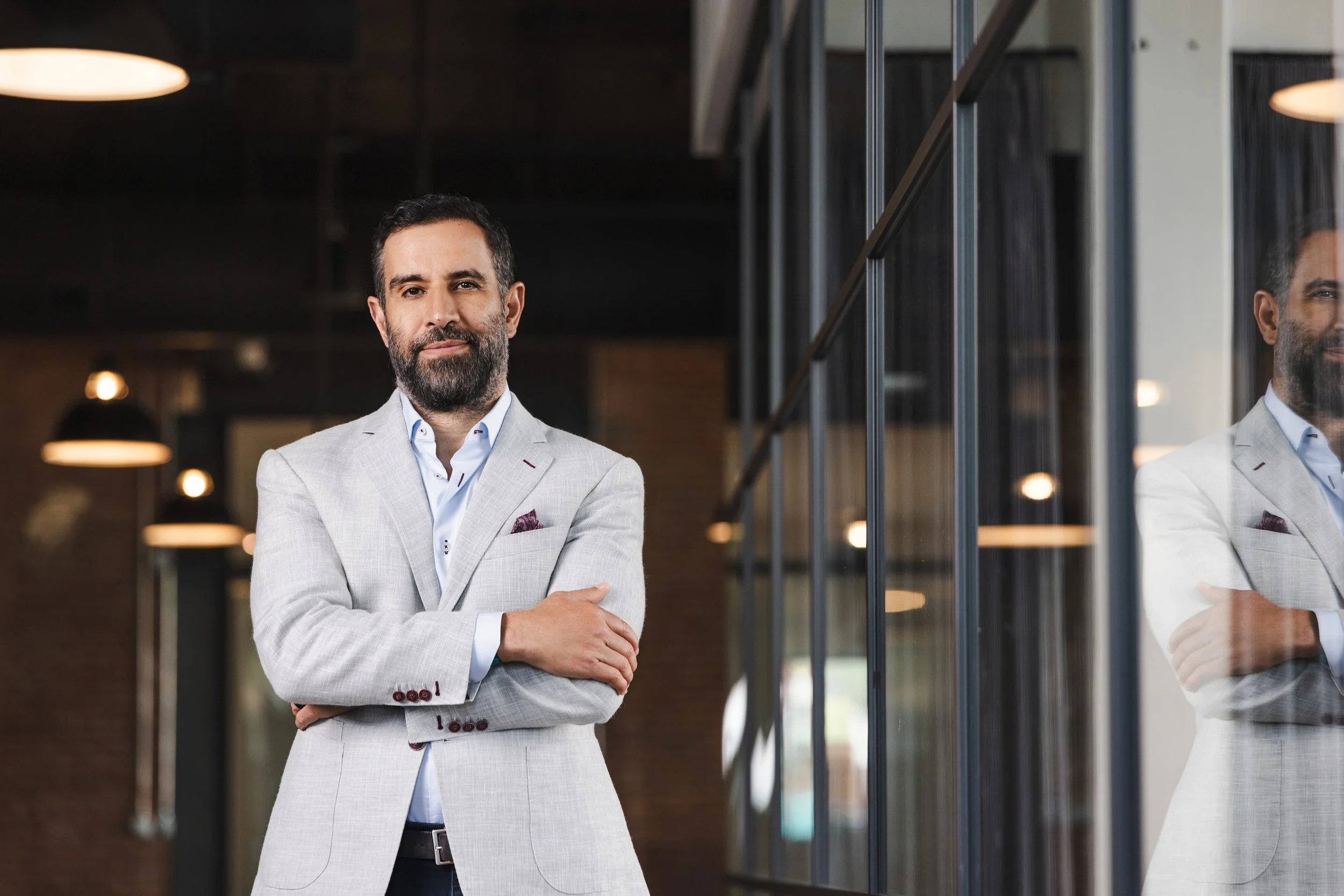 Executive headshot of man in grey suit with arms crossed standing in modern office with glass wall reflection, Nashville TN