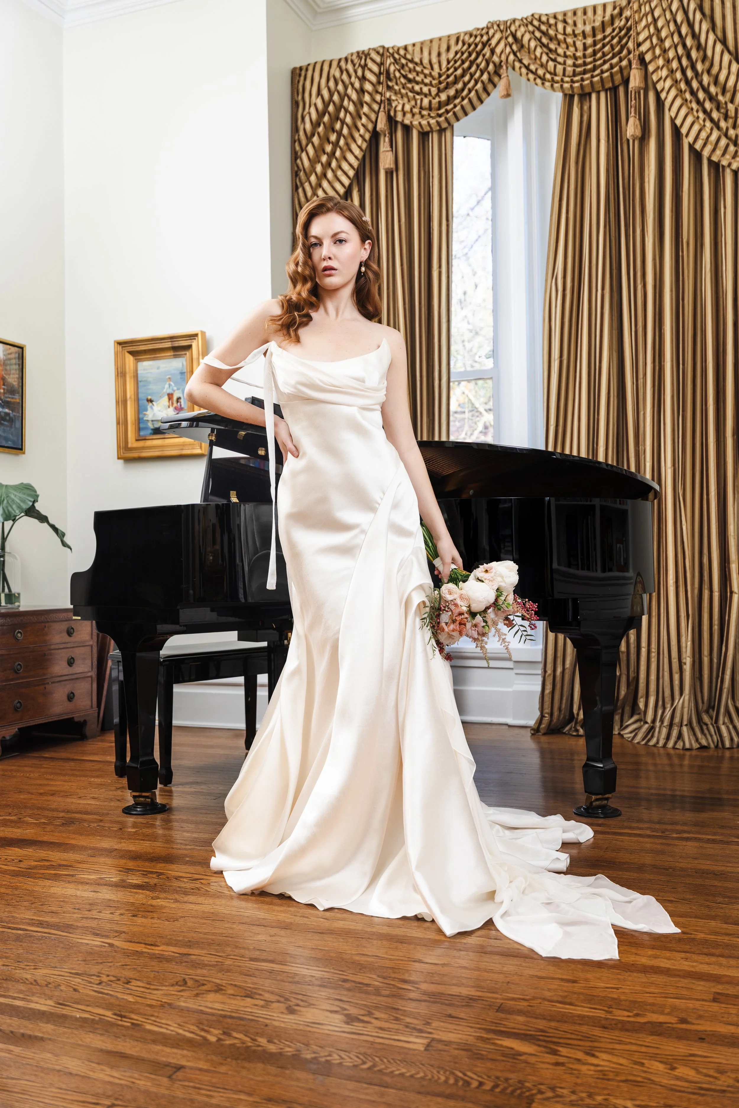 Bride in vintage-inspired satin gown poses by a grand piano with soft directional lighting, showcasing classic Hollywood glam hair and golden drapes