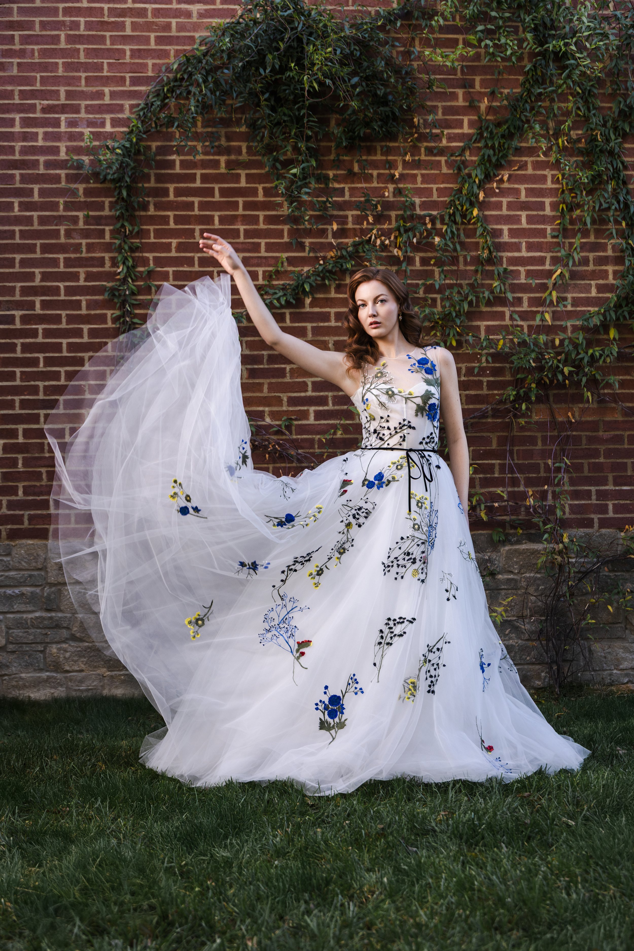 Bride lifts flowing embroidered gown for dynamic motion shot against textured brick and greenery at luxury Nashville venue