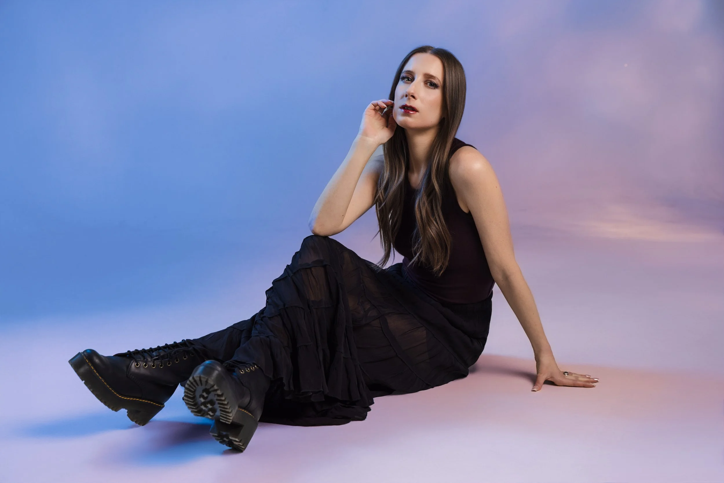 Seated studio portrait of Lauren River with blue and pink gel lighting reflected off mylar onto the wall using a two-light studio lighting setup.