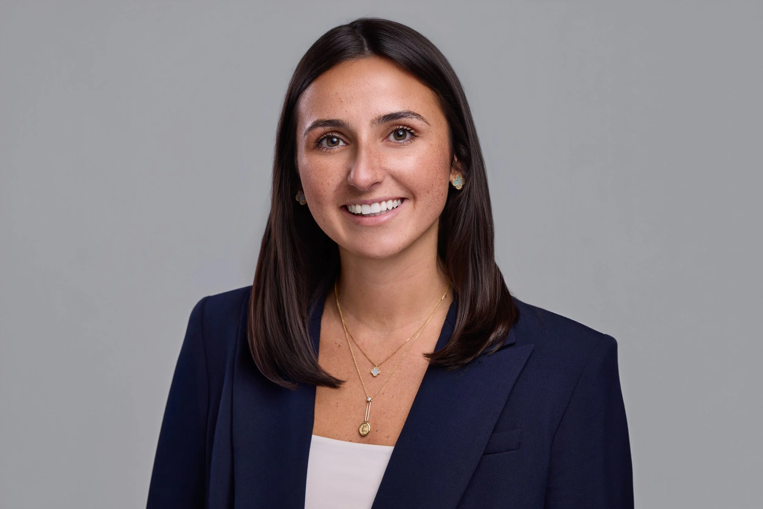 Professional LinkedIn headshot of a female executive in a navy blazer with soft, even lighting on a neutral gray background