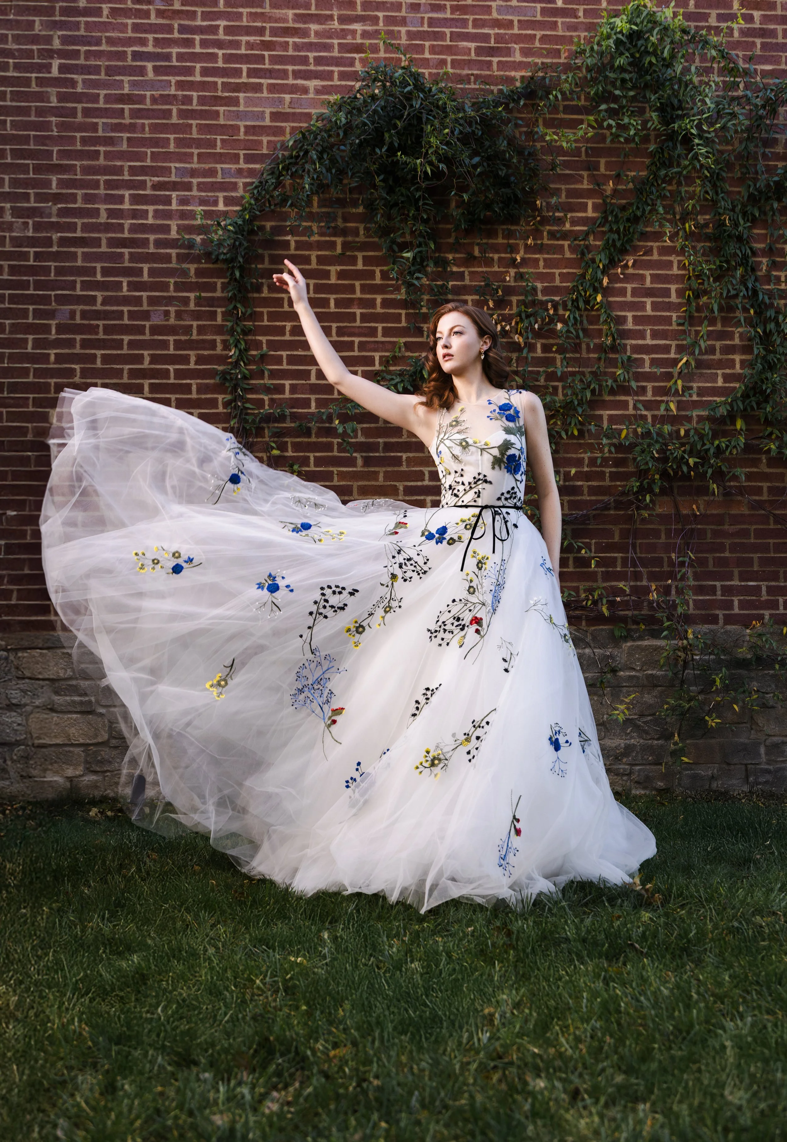 Bride in embroidered tulle gown tosses skirt mid-spin outside Watson House, framed by brick wall and ivy for romantic editorial moment