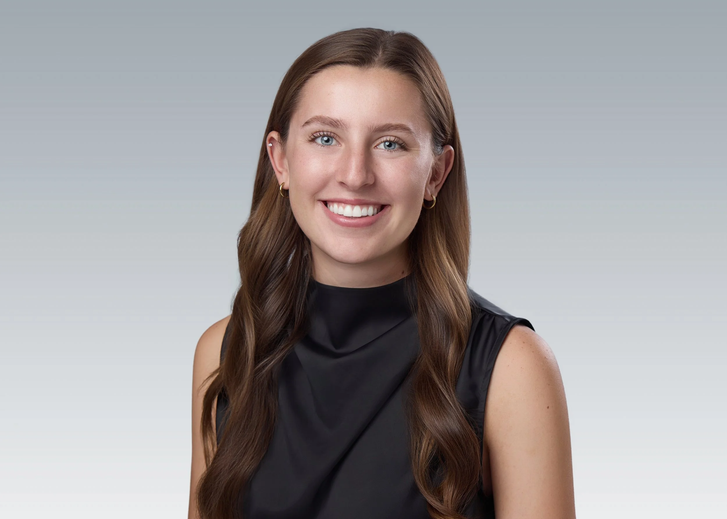 Professional team headshot of a smiling woman with long wavy hair in a black sleeveless top, consistent gray studio background, by Nashville headshot photographer Tausha Dickinson