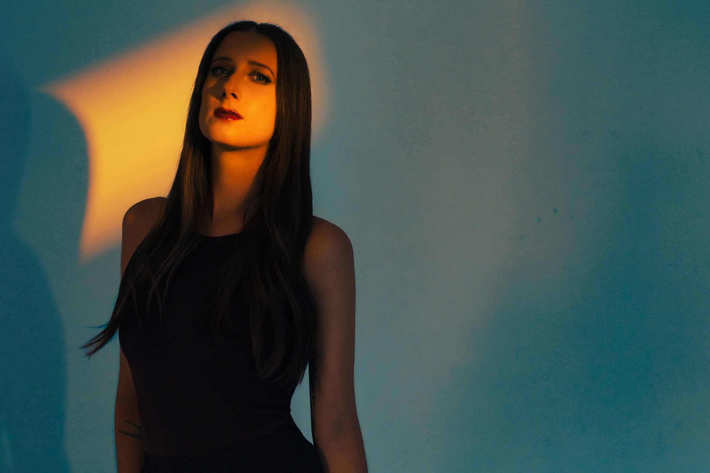 Close-up portrait of Lauren River with a narrow slice of orange gel light across her face and blue fill cooling the shadows in a two-light studio lighting setup.