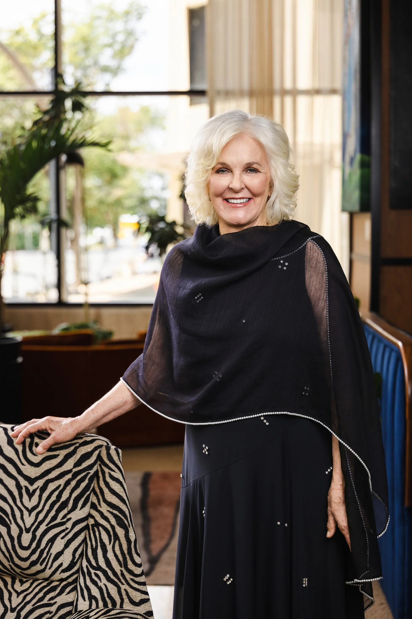 Trish Munro smiling beside the zebra print chair near a sunlit window at the Fairlane Hotel, Nashville.
