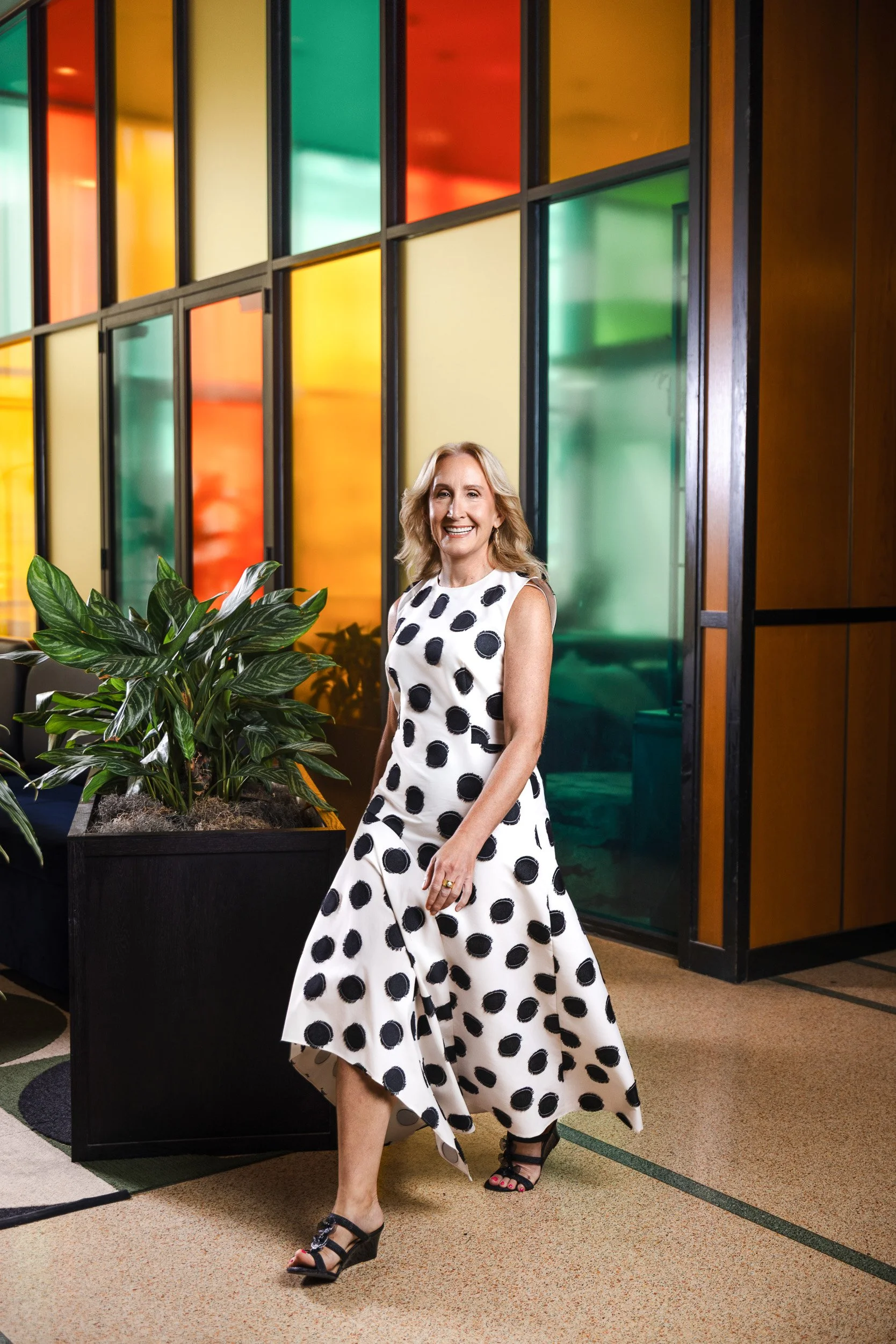 Jennifer Biefel walking past a colorful stained glass paneled wall in a black and white polka dot dress for her Nashville portrait session.